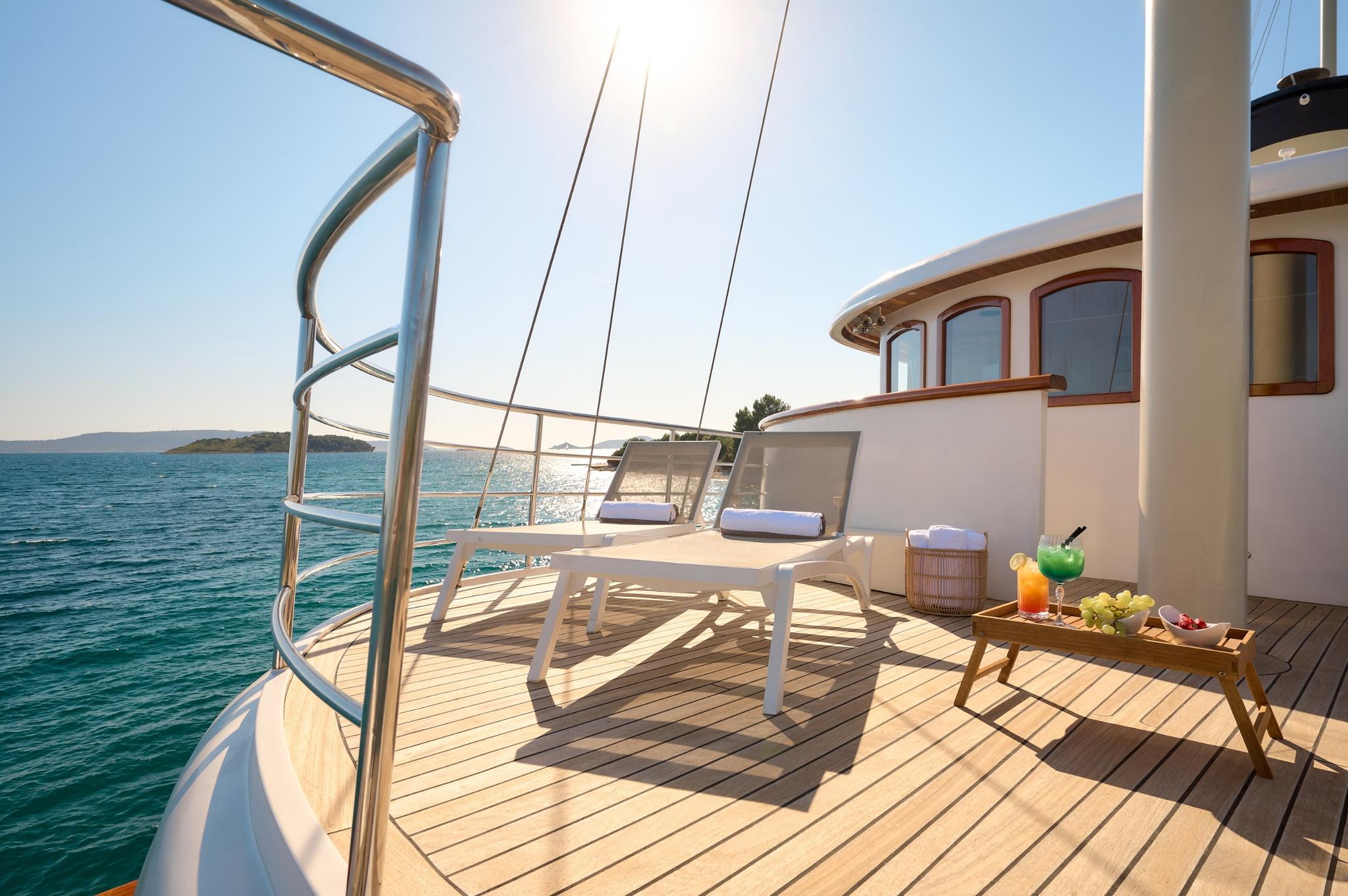 gulet bow deck with white sun loungers, breakfast tray, and coastal views