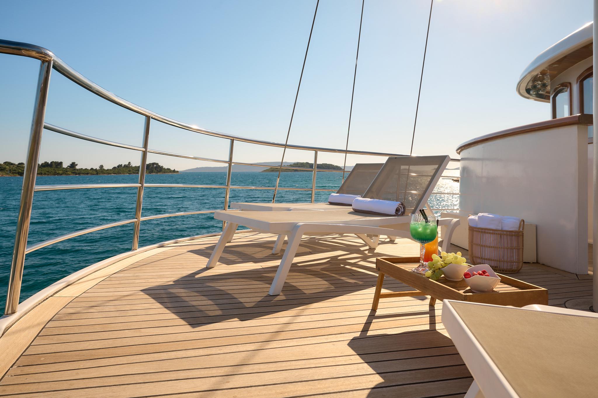 bow sun deck with white sun loungers, cocktails and fruit platter on wooden table