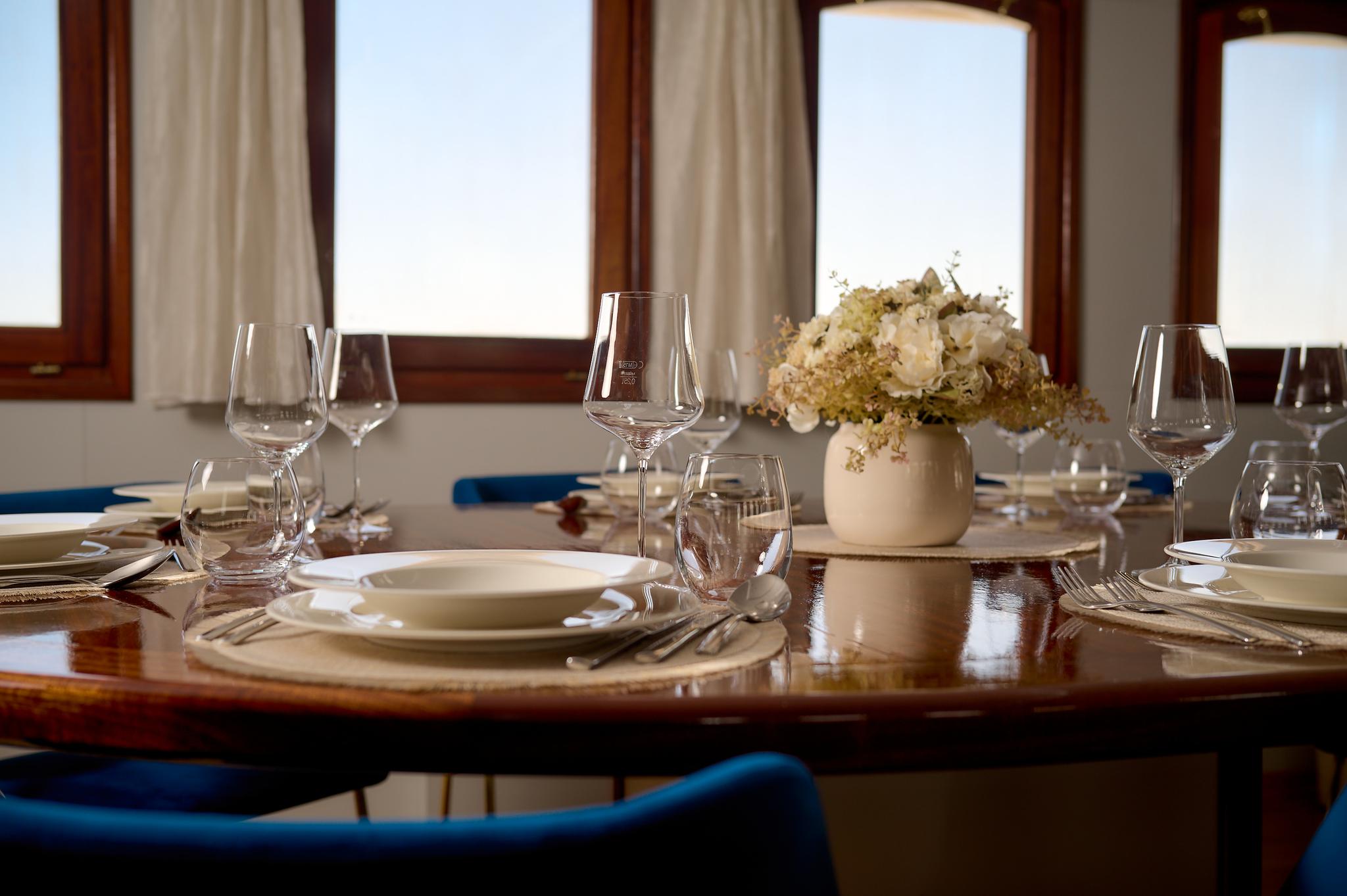 elegant yacht dining table set with wine glasses, plates, cutlery and white floral arrangement
