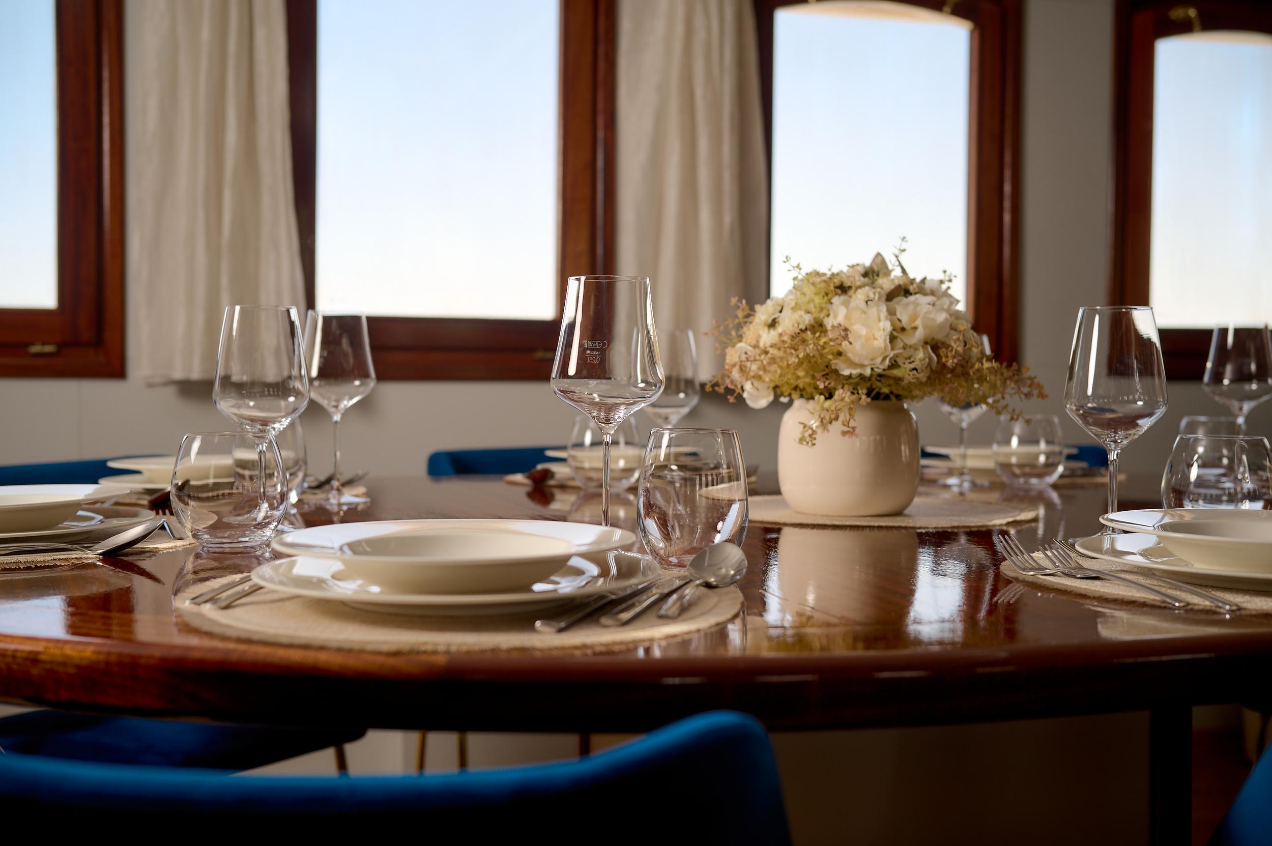 elegant yacht dining table set with wine glasses, plates, cutlery and white floral arrangement