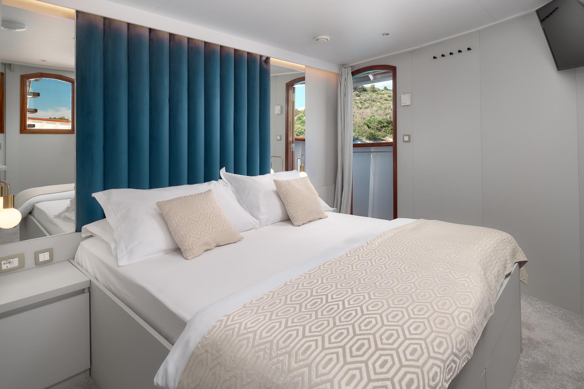 yacht guest cabin featuring double bed with blue upholstered headboard and portholes