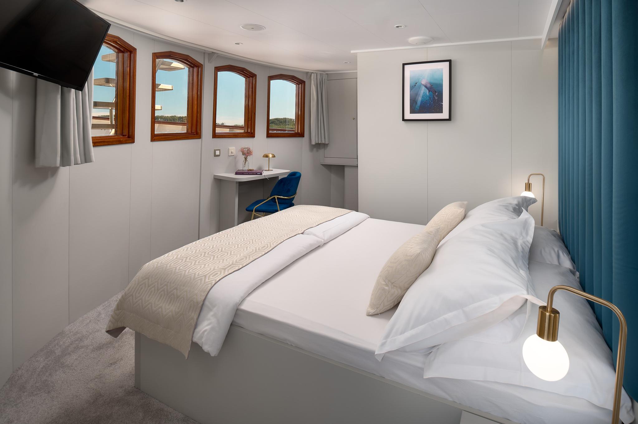 yacht guest cabin featuring double bed, four wooden-framed portholes, built-in desk with blue chair