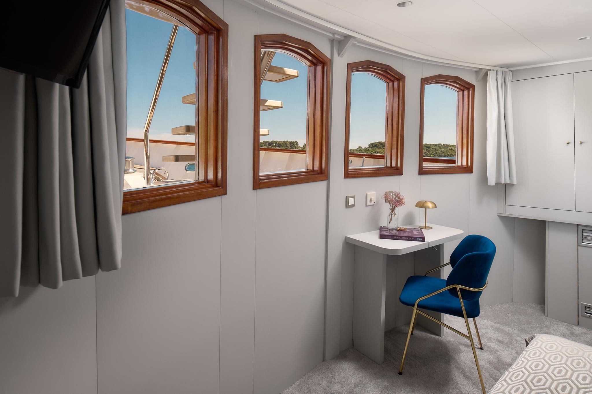 yacht cabin interior with built-in desk, blue velvet chair and panoramic windows