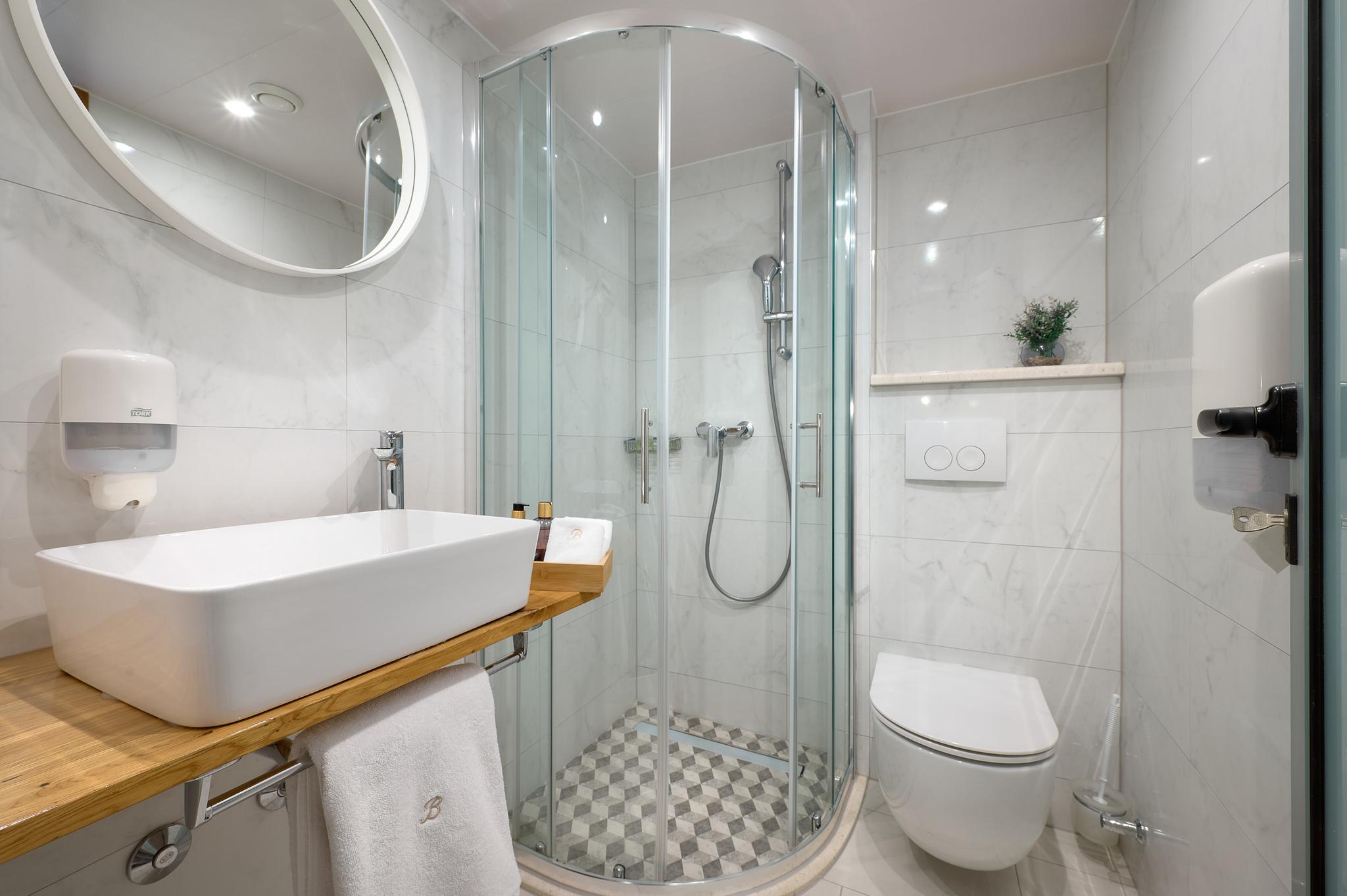 yacht bathroom featuring curved glass shower enclosure, vessel sink on wooden vanity, wall-mounted toilet