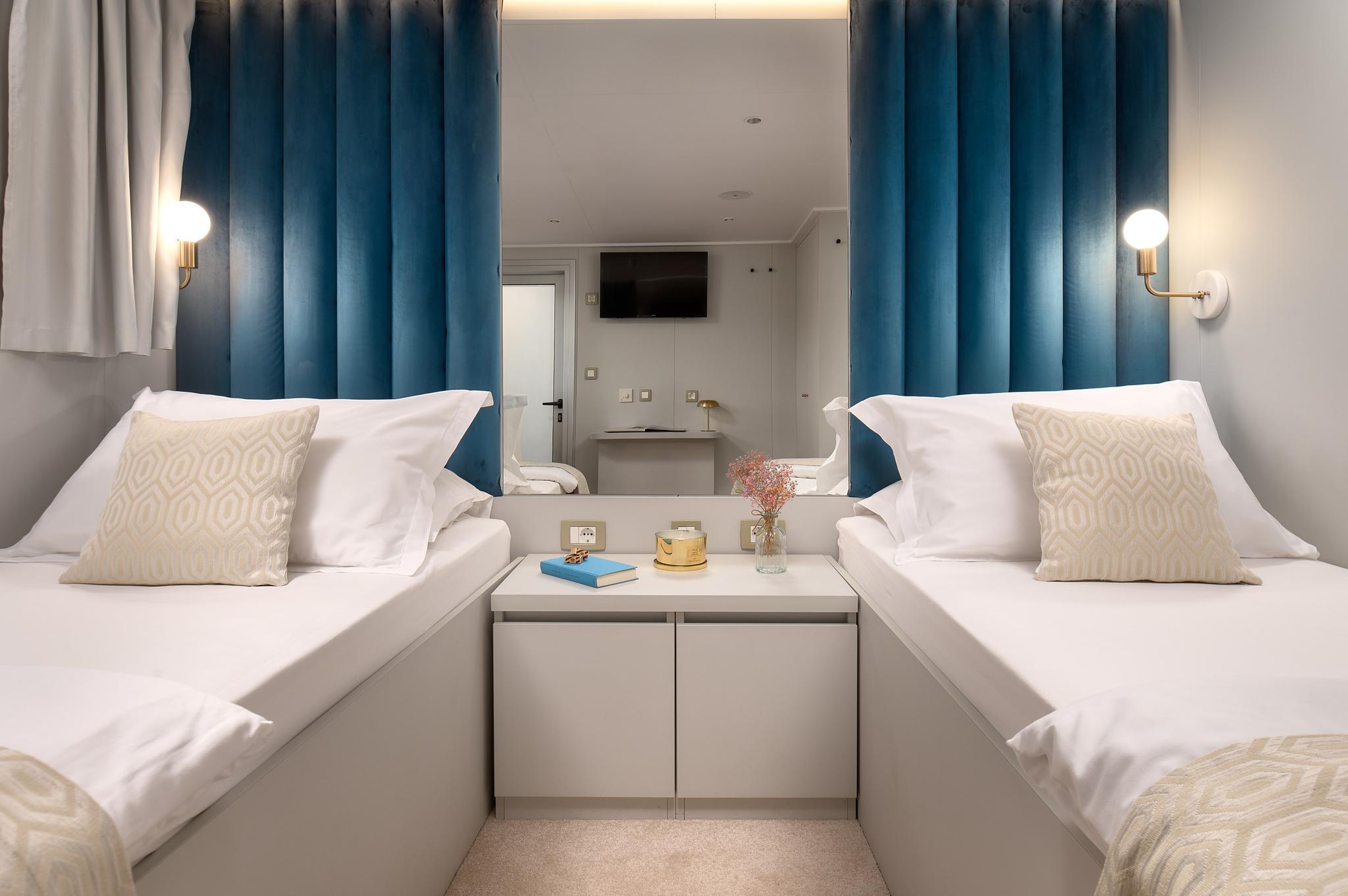 yacht twin cabin with white bedding, blue curtains, and central storage nightstand