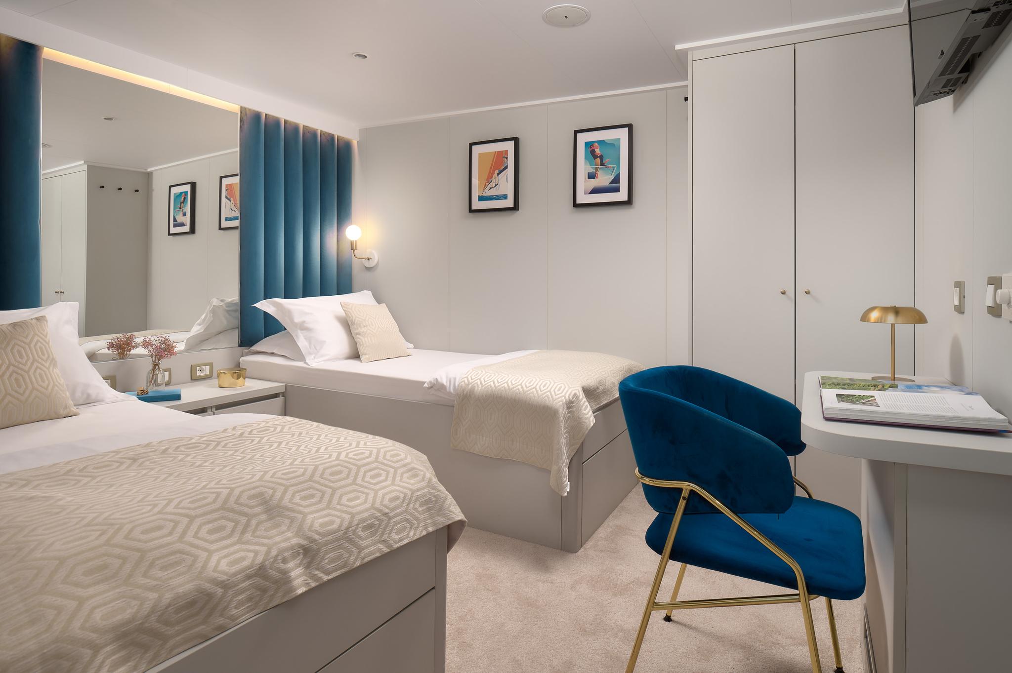 yacht twin cabin interior with two single beds, blue curtains, and nautical artwork