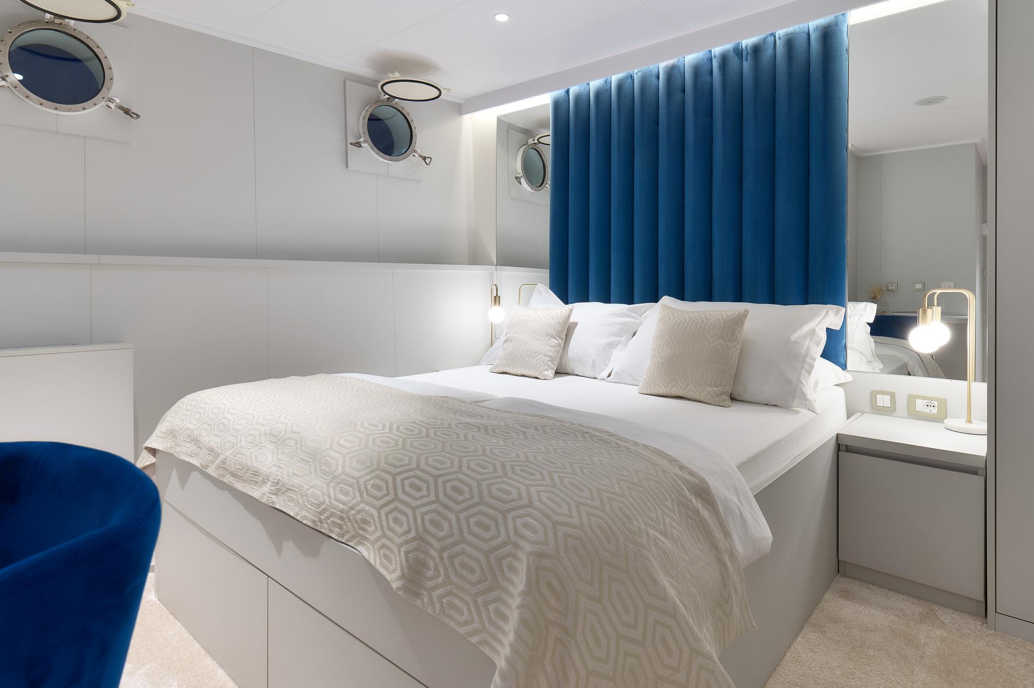 yacht guest cabin featuring double bed with geometric bedding and circular portholes