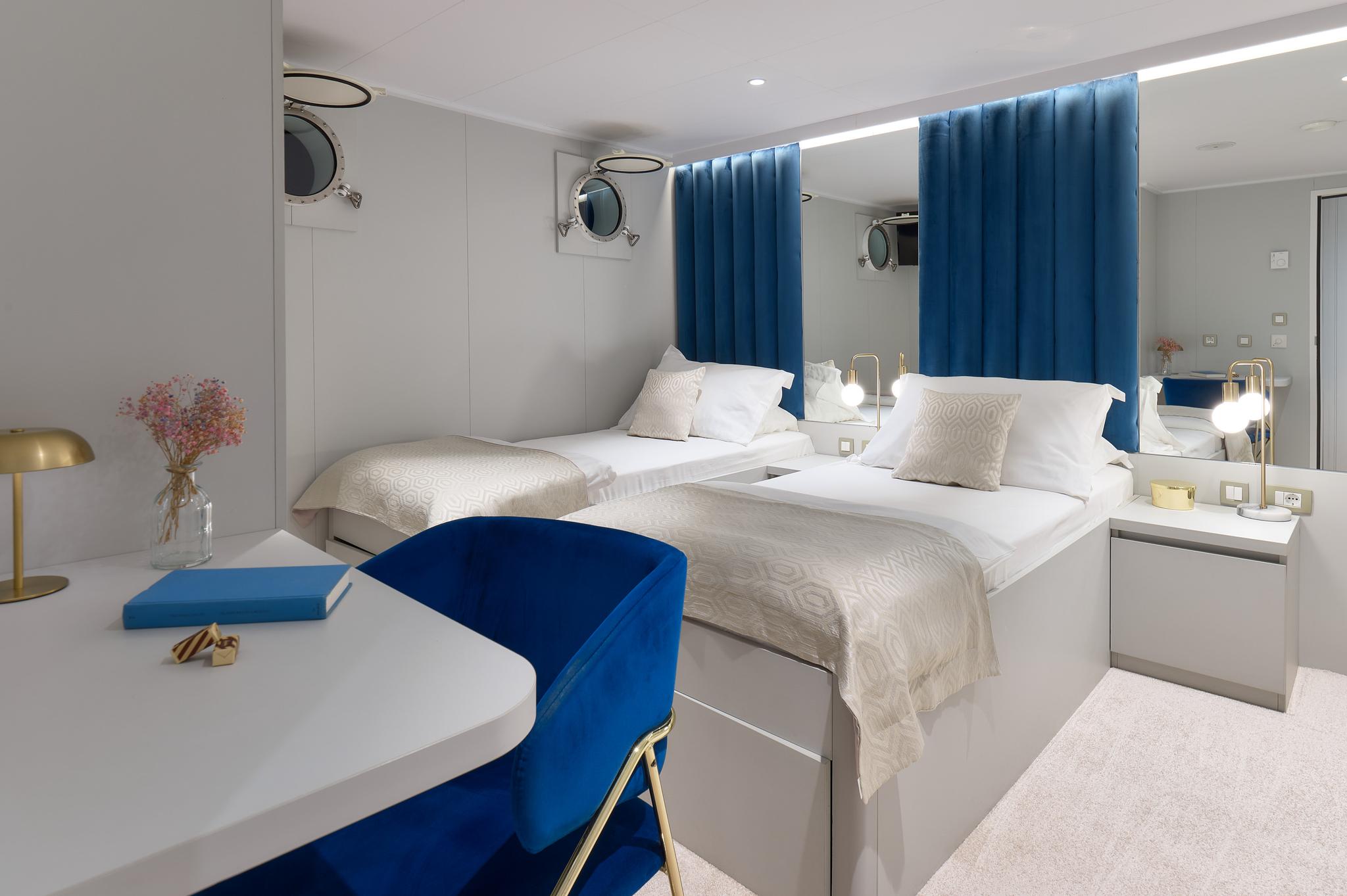 luxury yacht guest cabin with twin beds, blue curtains, nautical mirrors and white furnishings