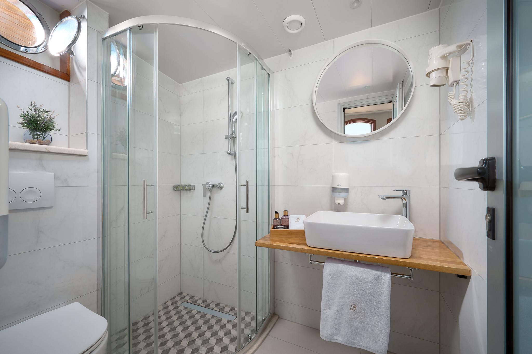 yacht ensuite bathroom featuring glass shower enclosure, vessel basin on wooden countertop, and circular mirror