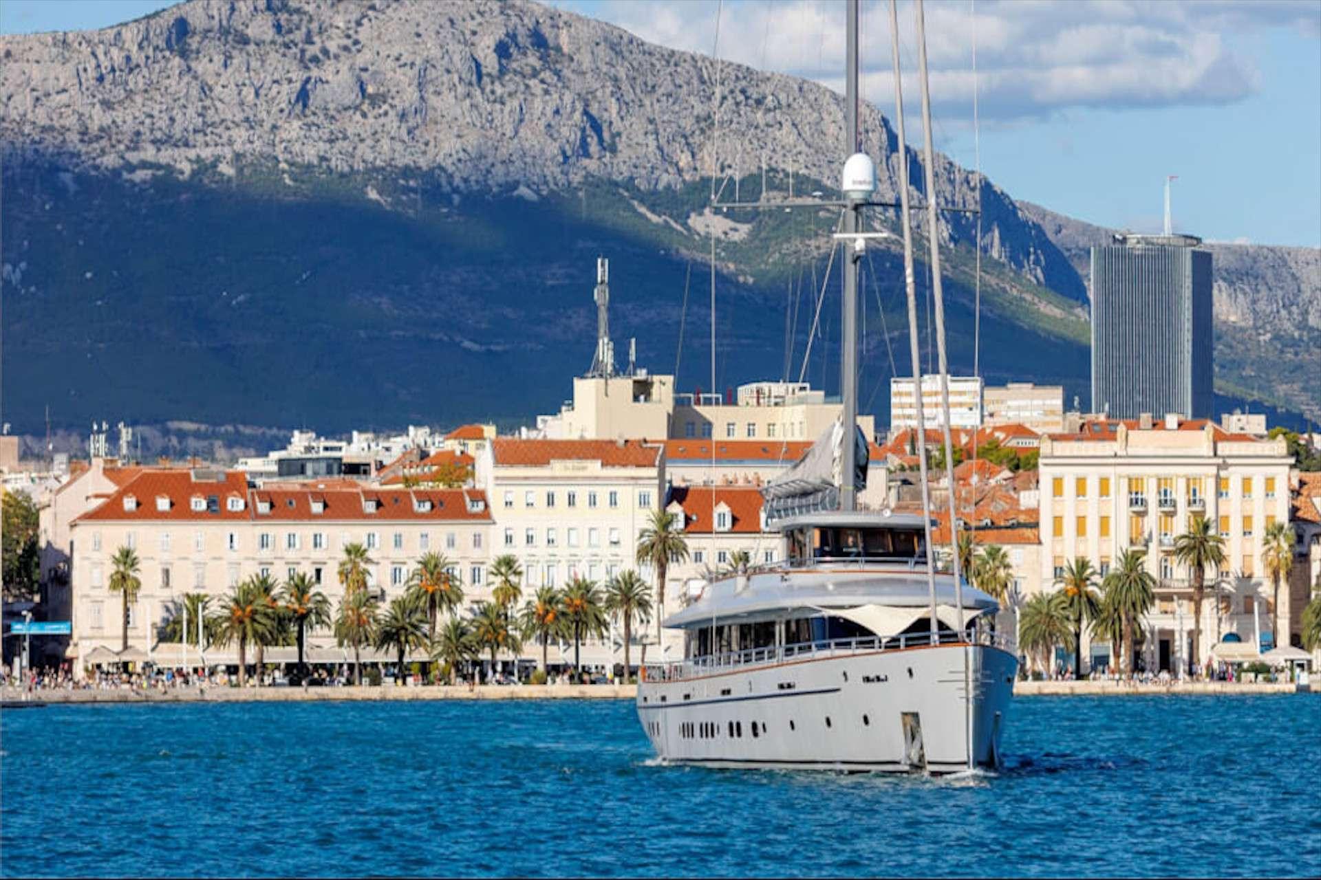 Luxury motor yacht with tall mast cruising Split harbour with Mosor mountain backdrop