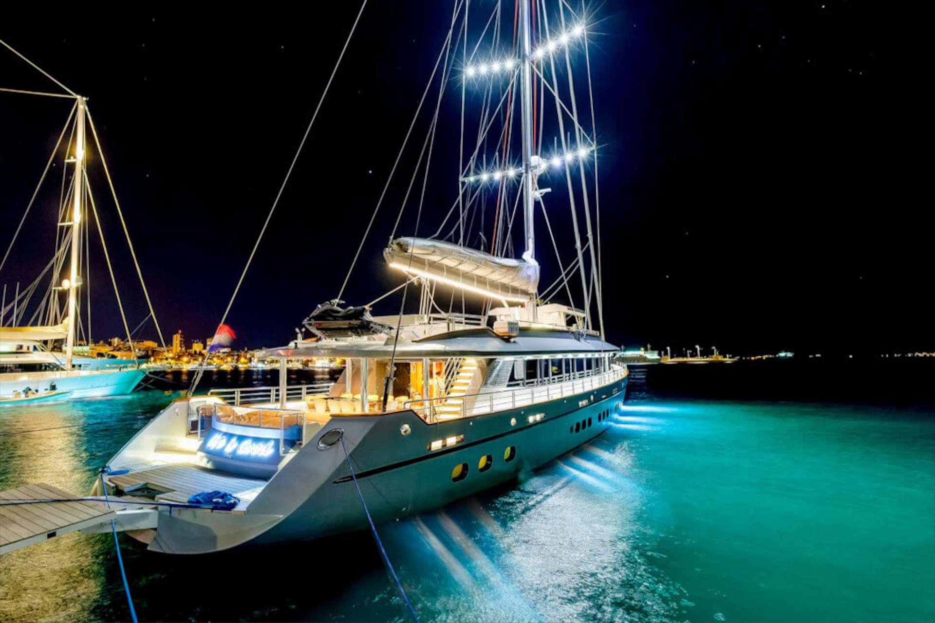 luxury sailing gulet moored at night with underwater lights glowing turquoise and neon stern name sign