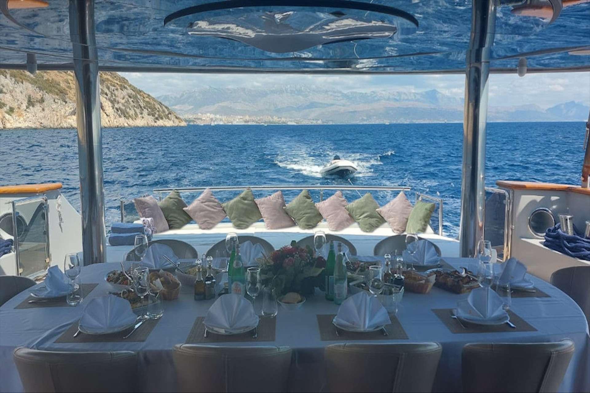 Luxury gulet aft deck dining table set with food, glassware, and floral centrepiece, tender visible underway behind