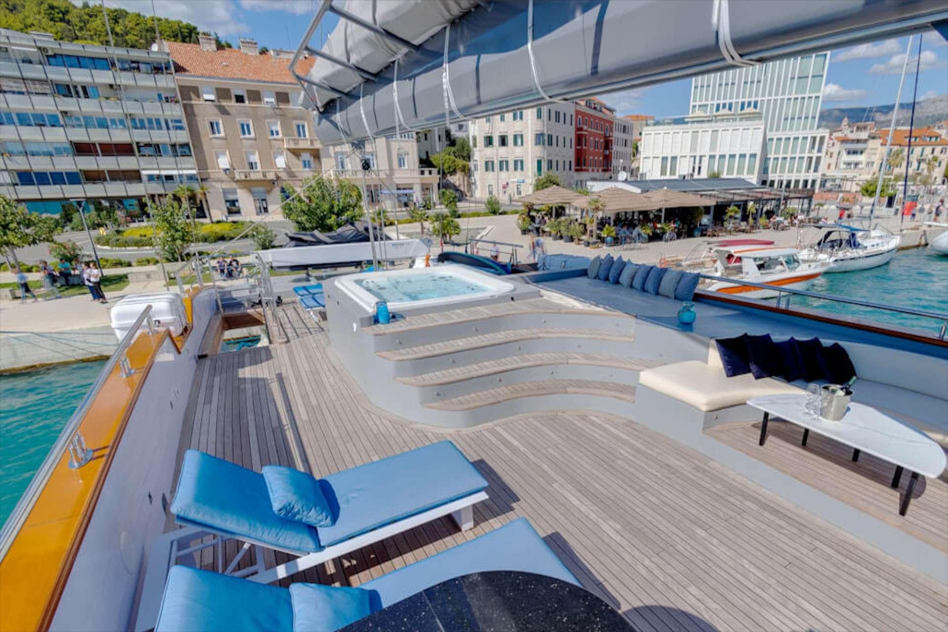 luxury gulet sun deck featuring built-in jacuzzi with curved steps, blue sun loungers, and harbour views