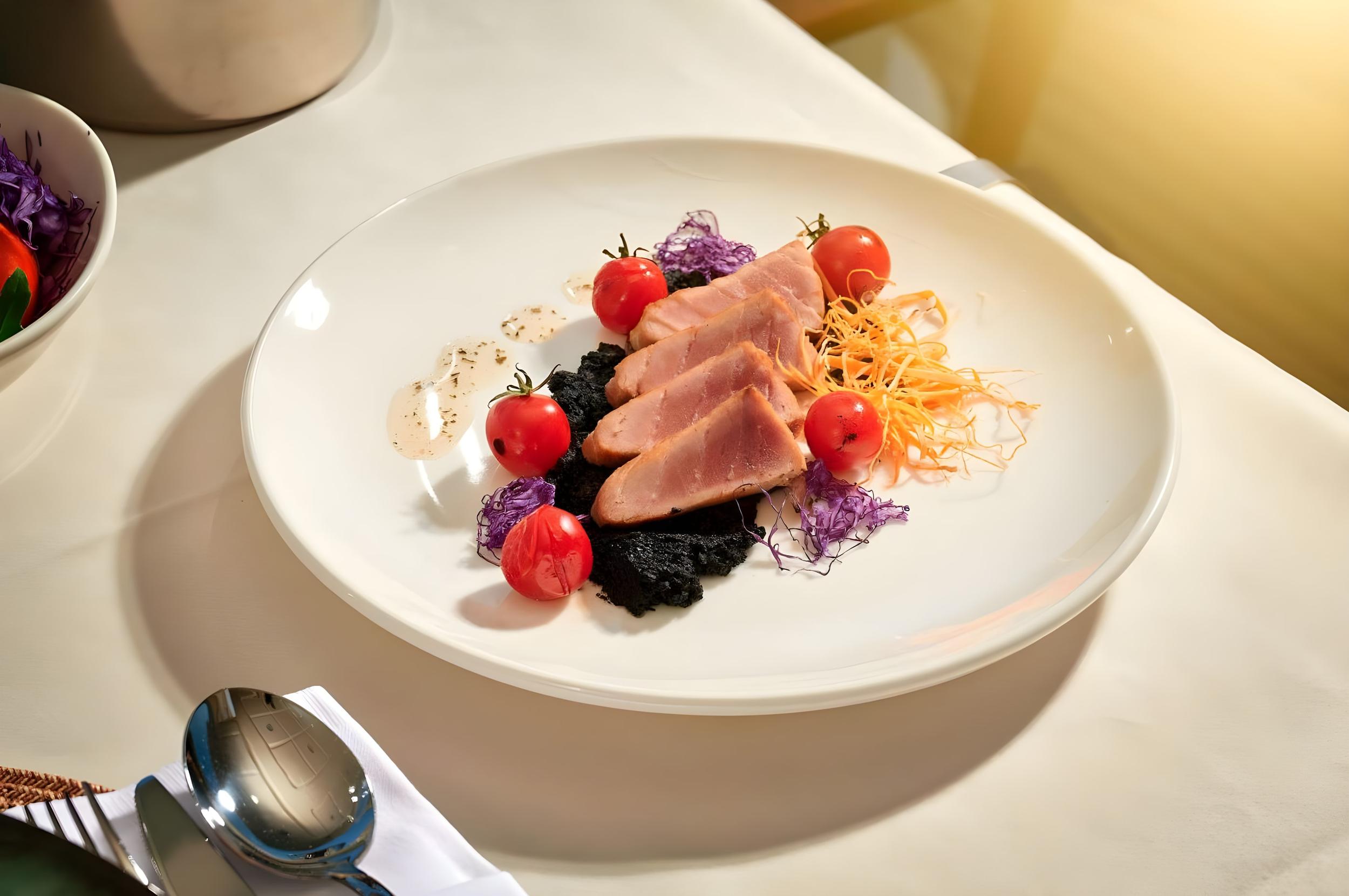 Fine dining plate of seared tuna on squid ink with cherry tomatoes and julienne carrots served on luxury yacht