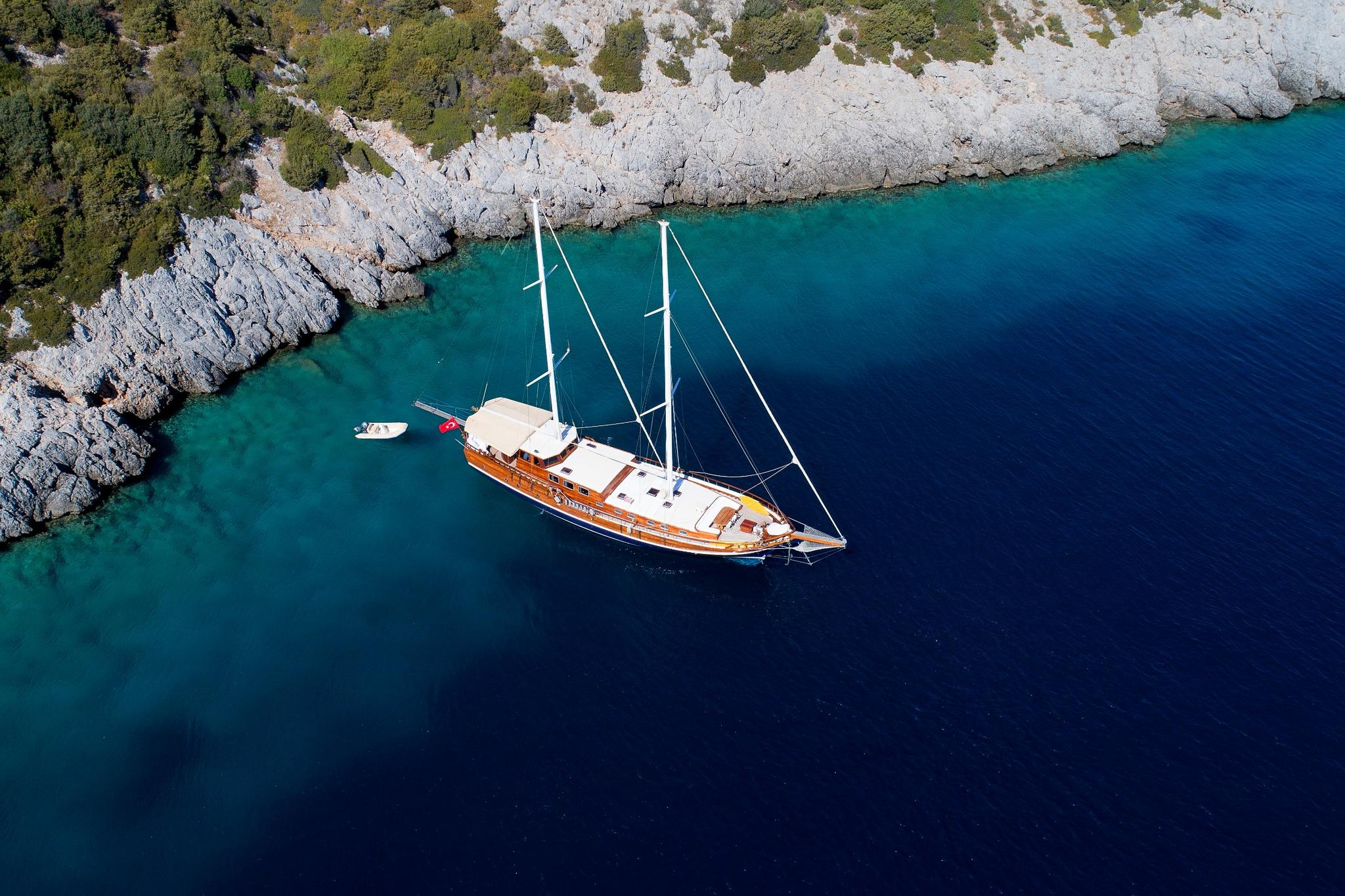 aerial view of traditional wooden gulet yacht anchored in crystal clear turquoise bay with rocky coastline
