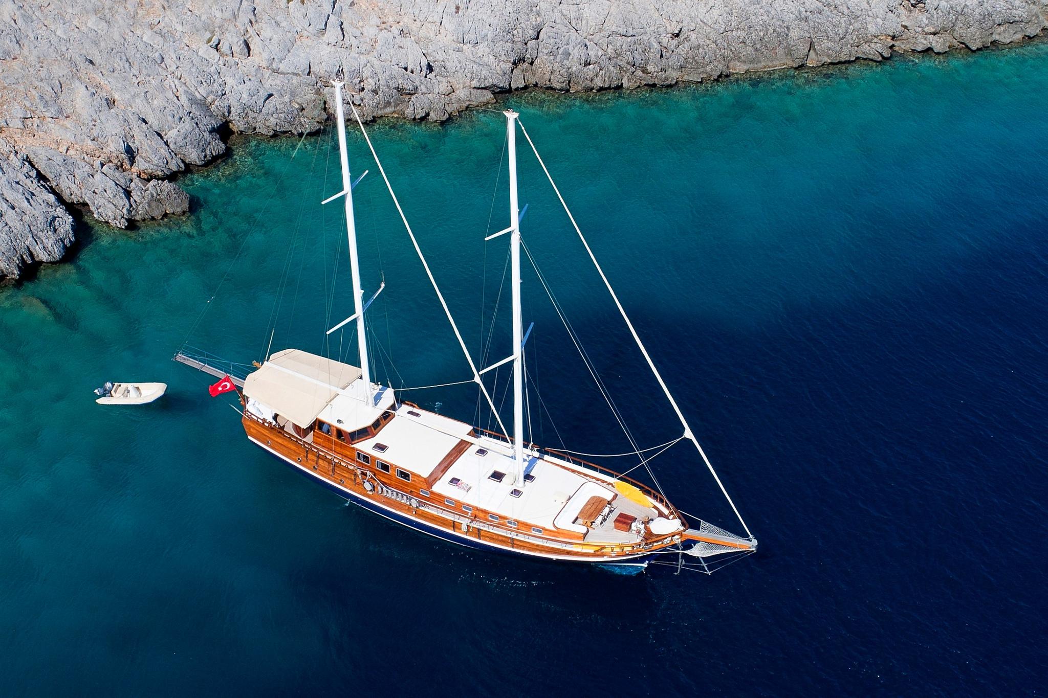 aerial view of traditional wooden gulet yacht with two masts anchored in crystal clear turquoise waters