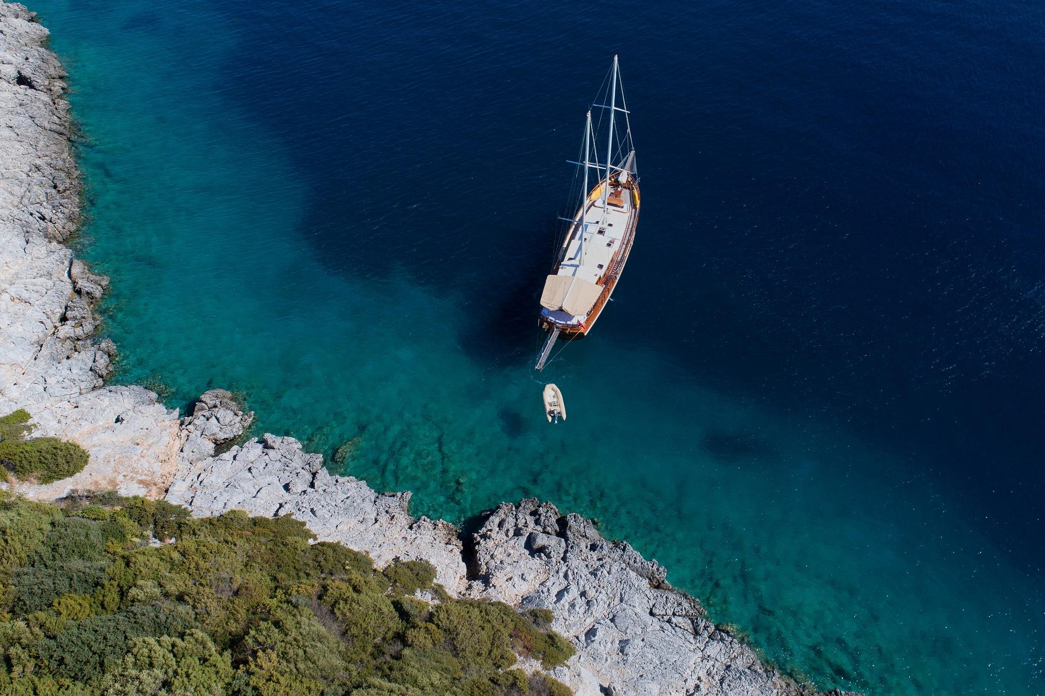 aerial view of traditional gulet yacht anchored in crystal clear turquoise bay with rocky coastline