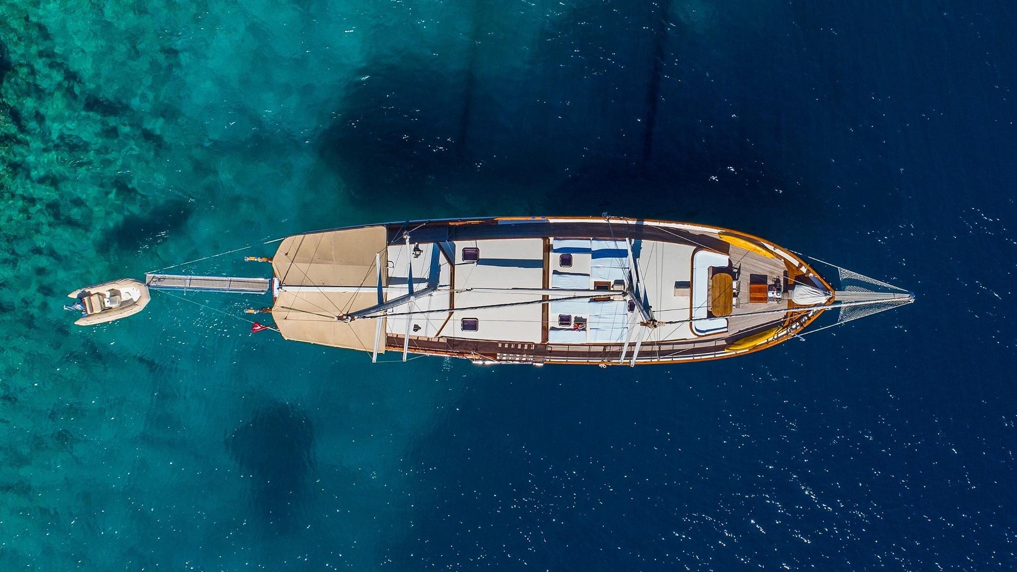 aerial view of white gulet yacht at anchor in crystal clear turquoise waters with tender boat nearby