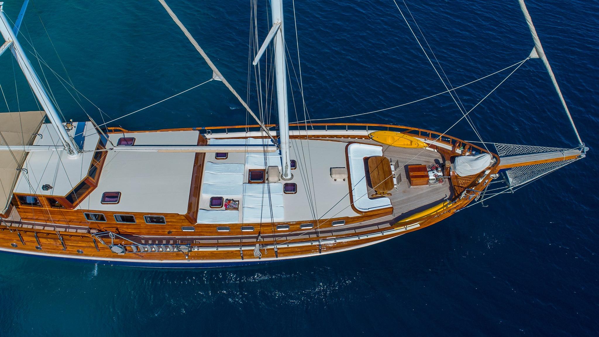 aerial view of wooden gulet yacht with white deck and rigging anchored in blue water
