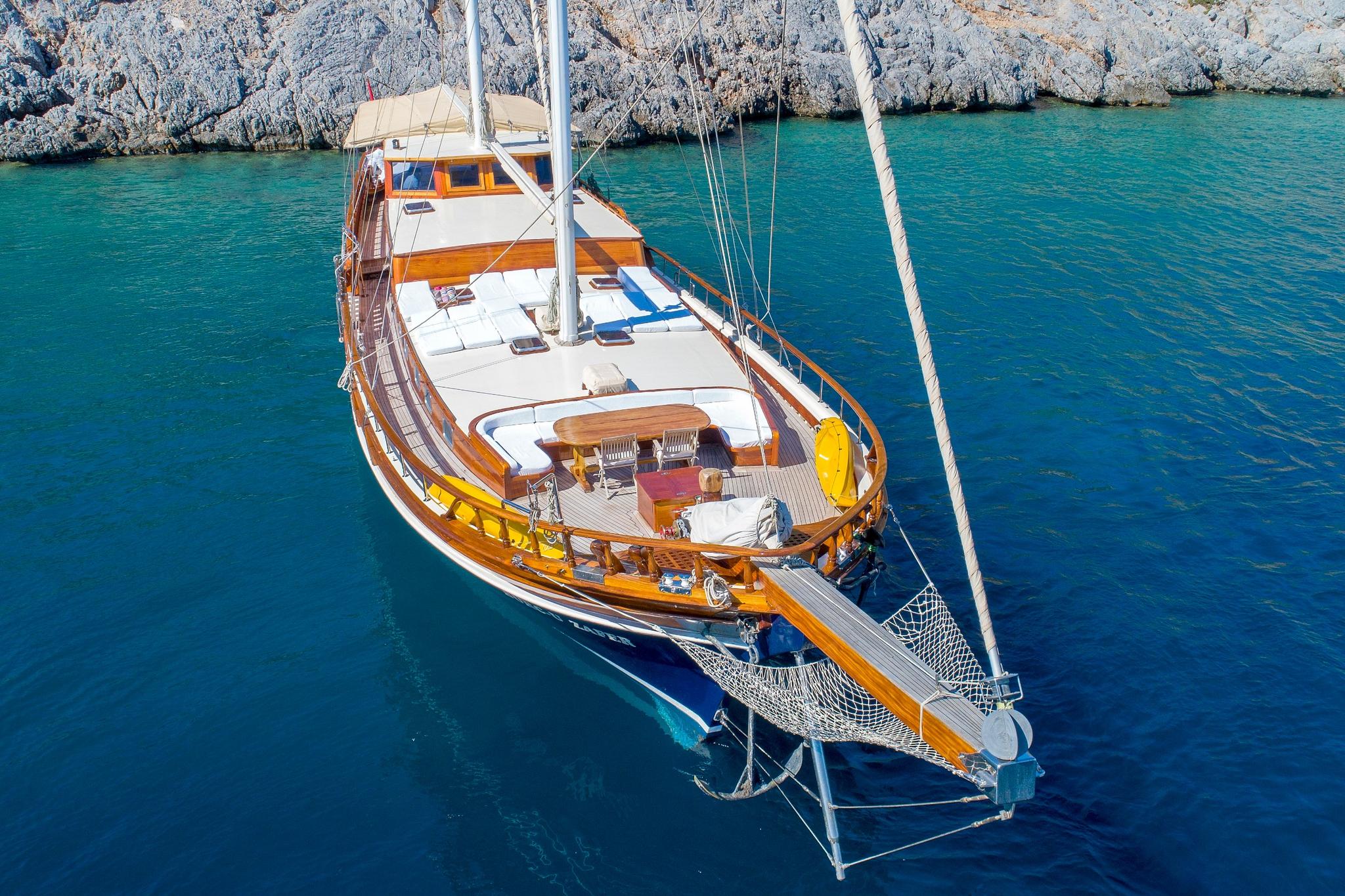 aerial view of traditional wooden gulet yacht anchored in crystal clear turquoise Mediterranean waters near rocky coastline