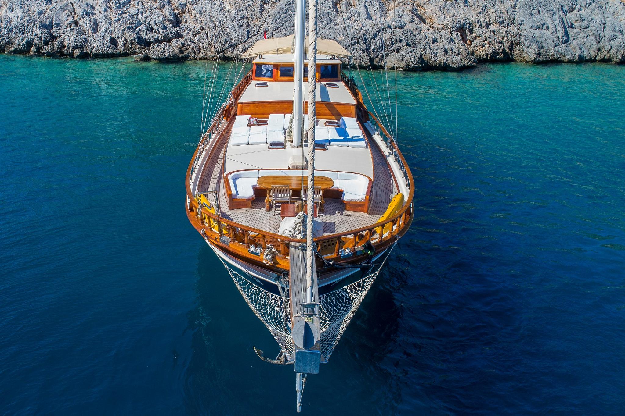aerial view of wooden gulet yacht with white sails anchored in crystal clear turquoise waters near rocky coastline