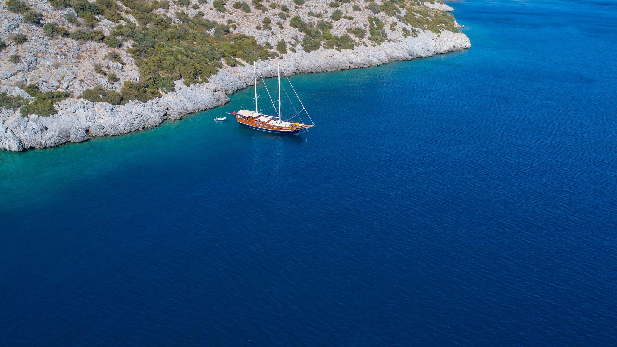 aerial view of traditional wooden gulet yacht anchored in pristine turquoise bay near rocky coastline