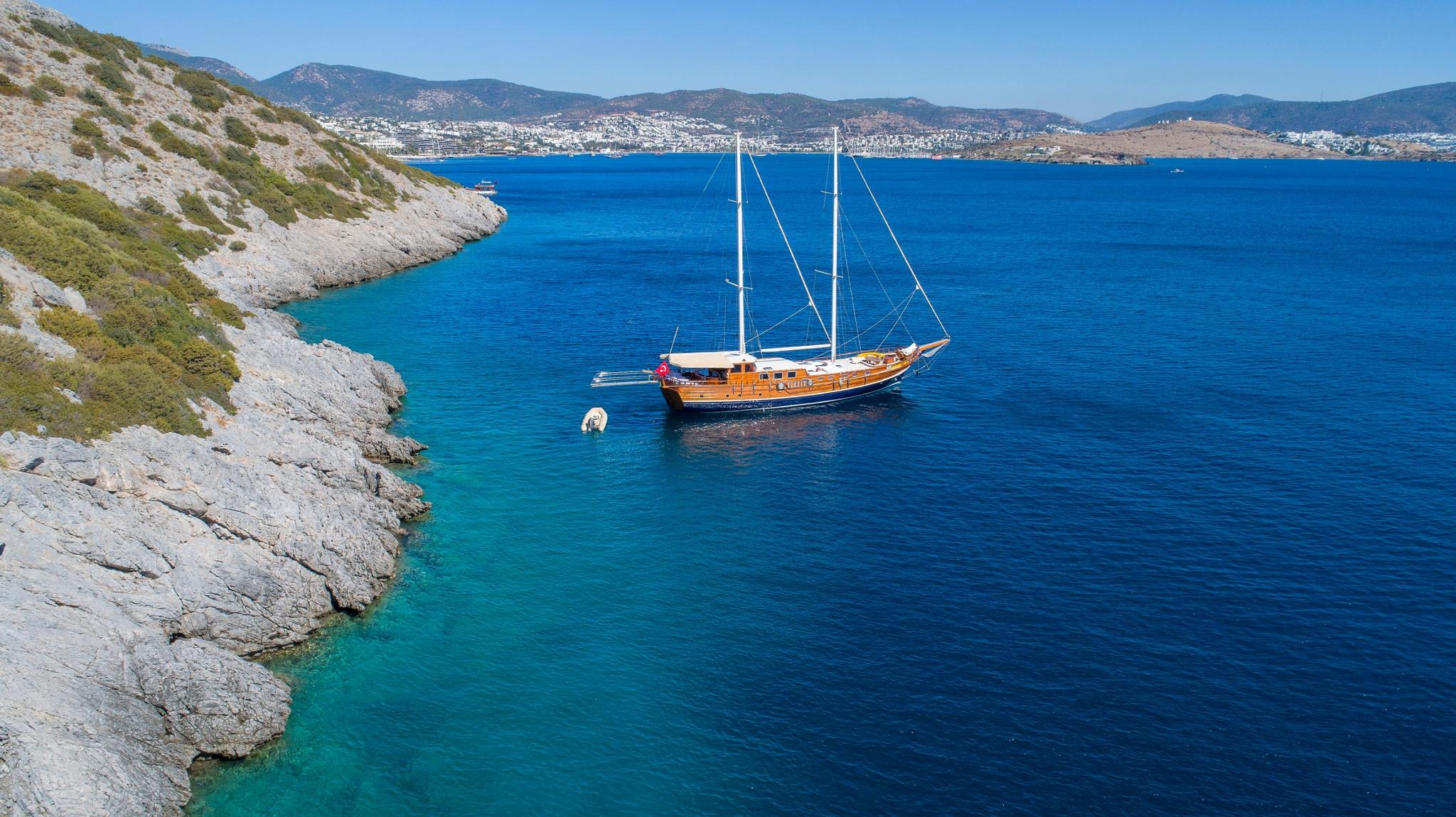 Aerial view of traditional wooden gulet yacht anchored in crystal clear turquoise bay with rocky coastline