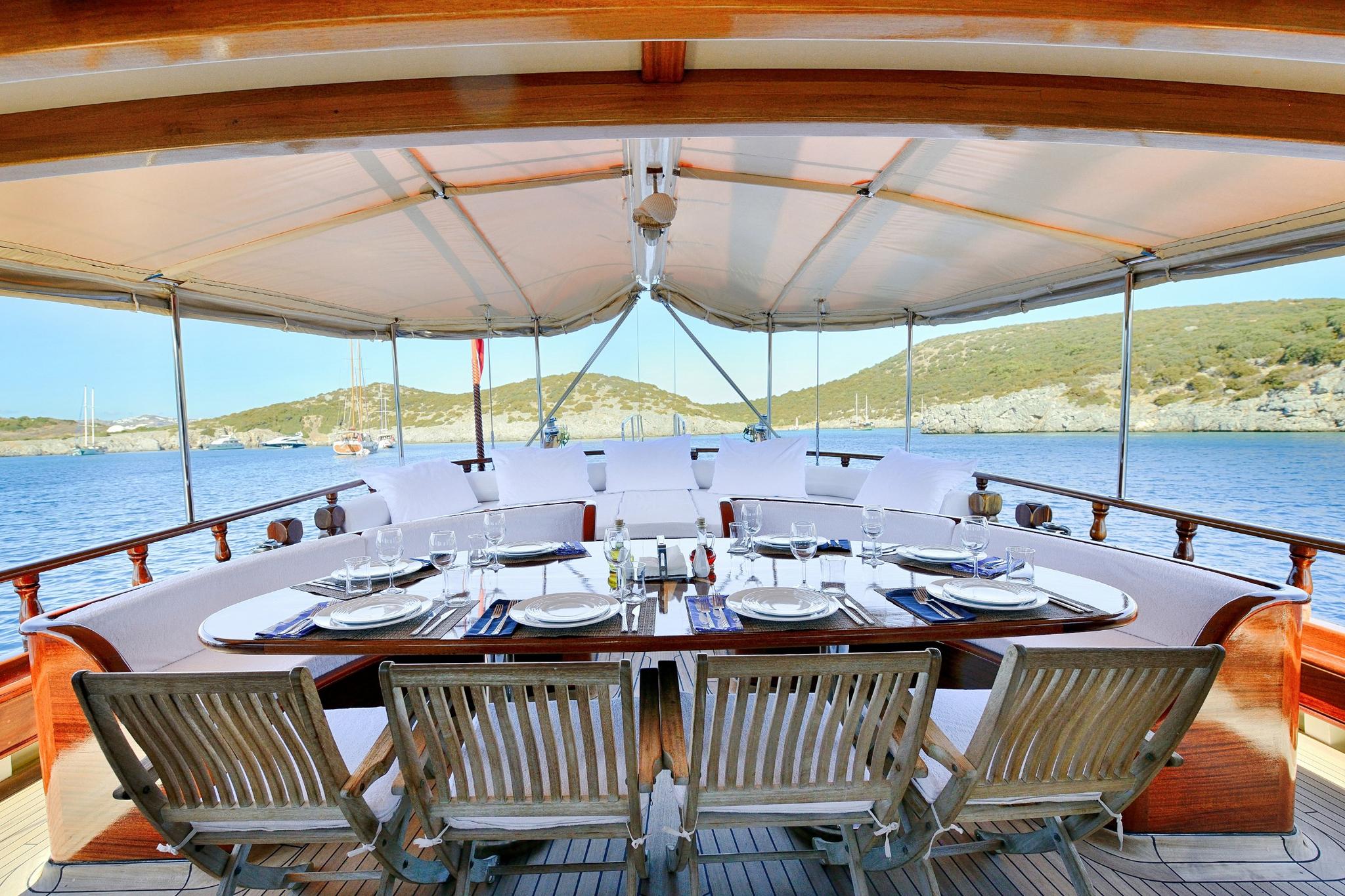 luxury gulet aft deck dining table with white plates wine glasses and teak chairs