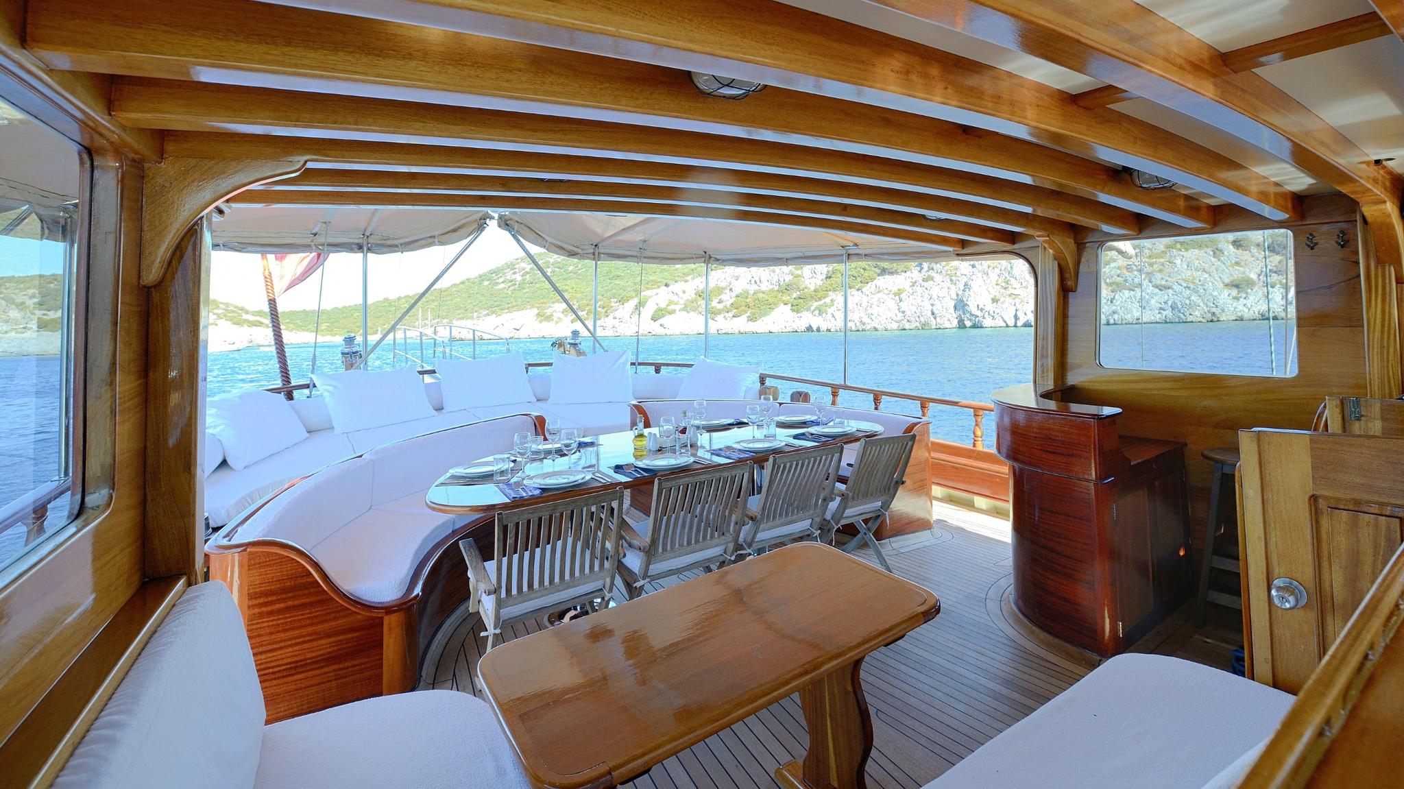 covered aft deck dining area with wooden table, teak chairs and scenic coastal views