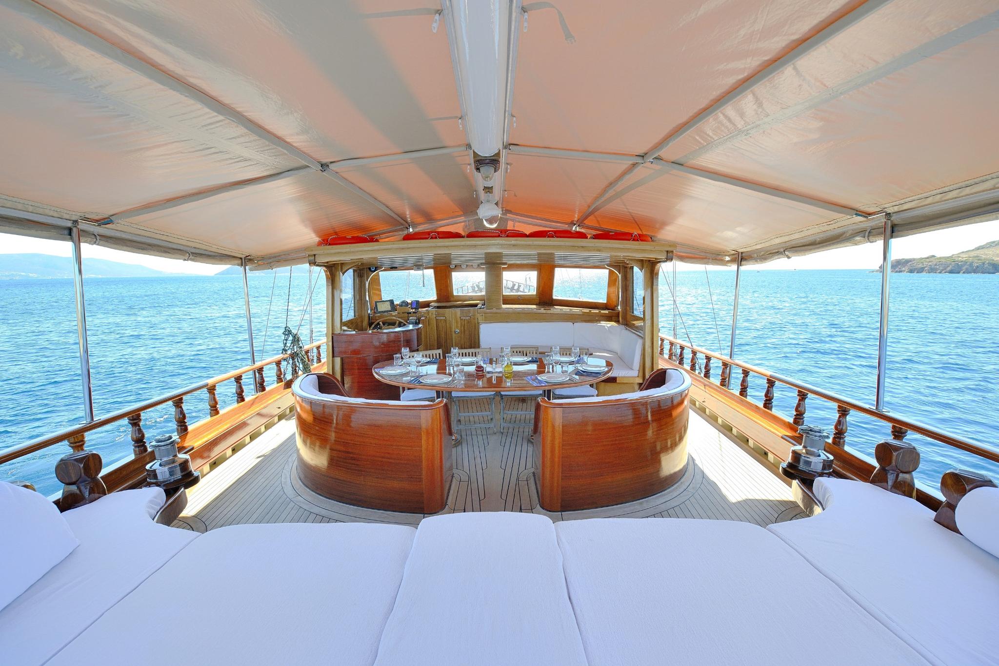 gulet aft deck with curved mahogany dining banquette, white table setting under canvas awning