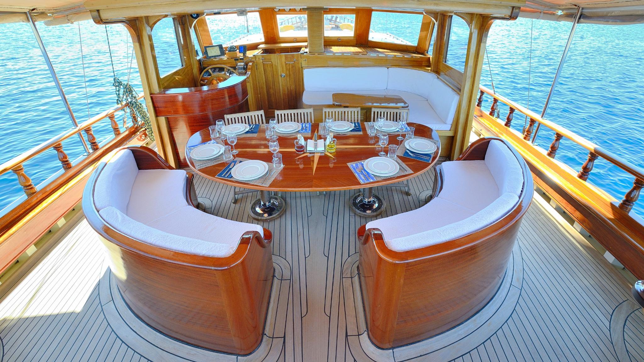 gulet aft deck with curved banquette seating around polished wood dining table set for eight