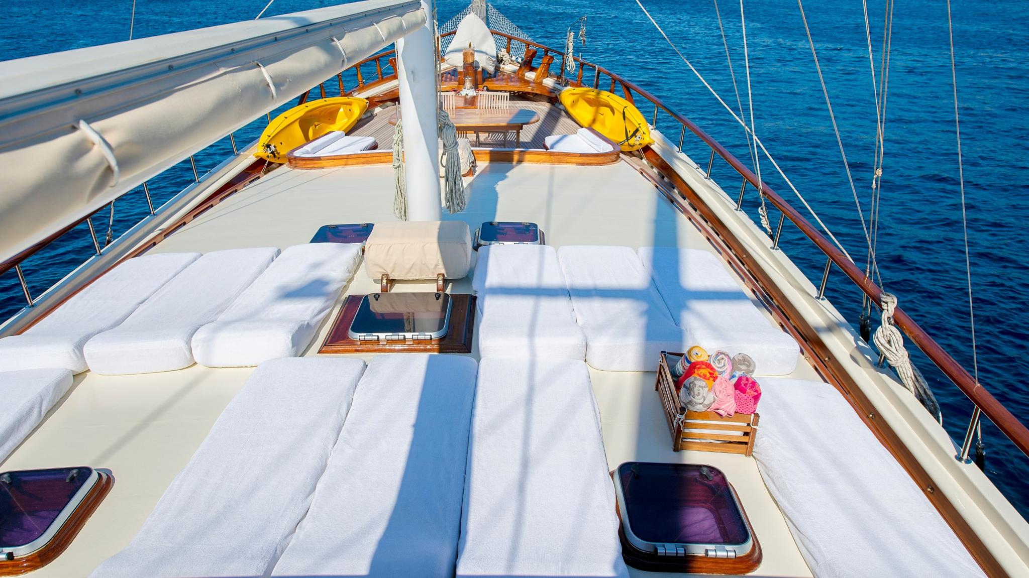 gulet bow deck with white cushioned sunbeds, wooden storage compartments and sailing mast