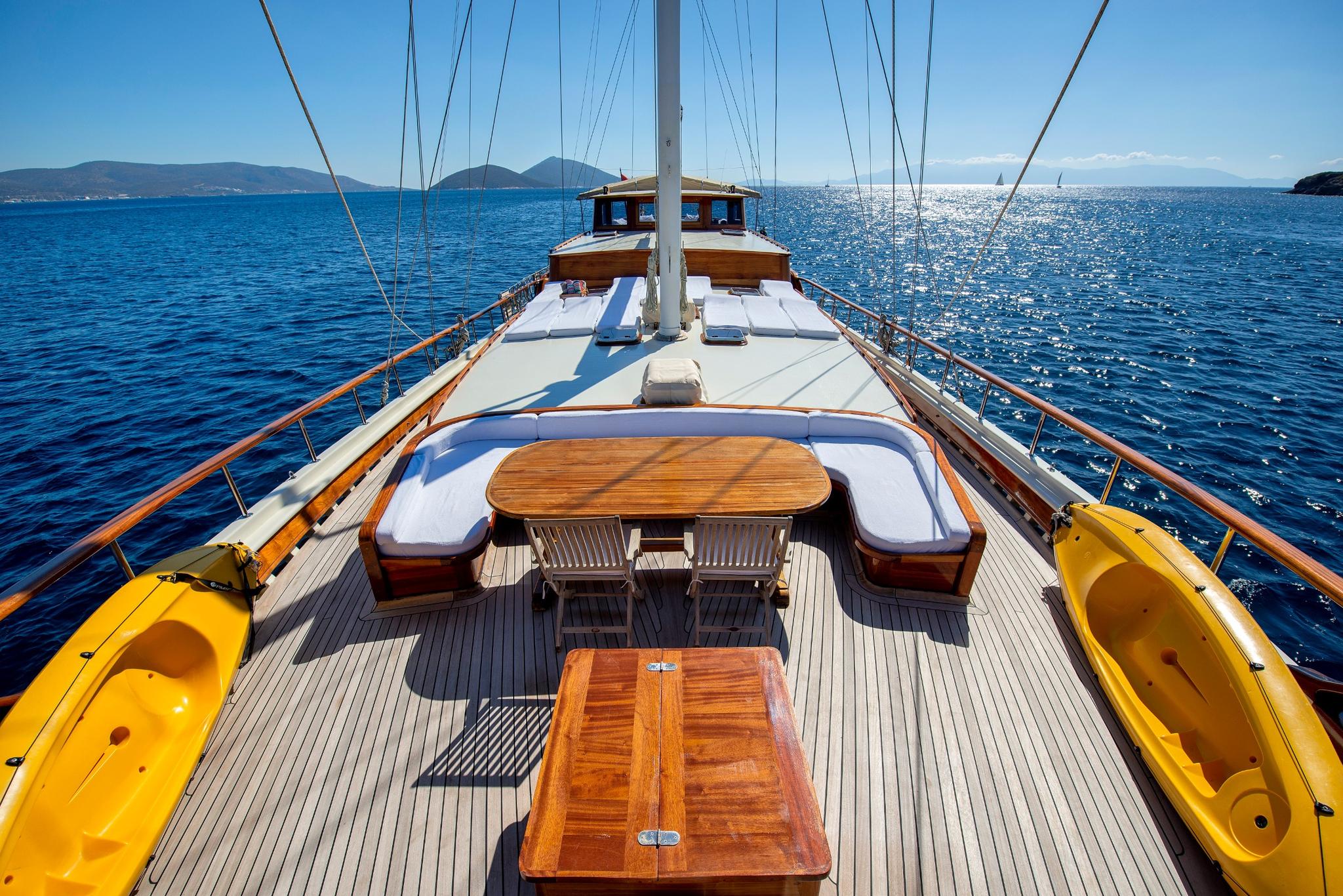 Forward deck of luxury gulet with curved seating, wooden dining table, and teak decking