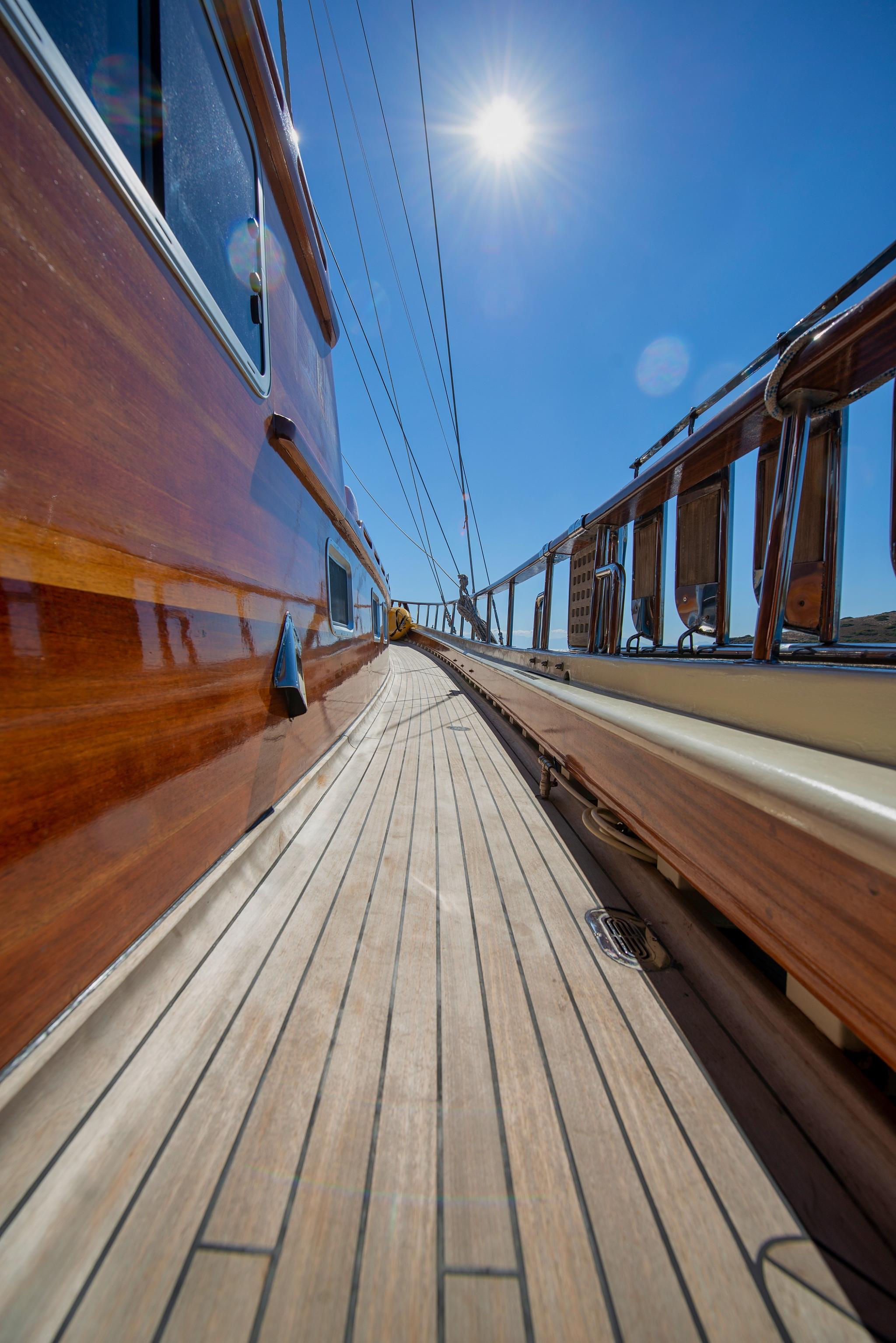 Yacht side deck walkway with teak planking, white hull, and rigging under blue sky
