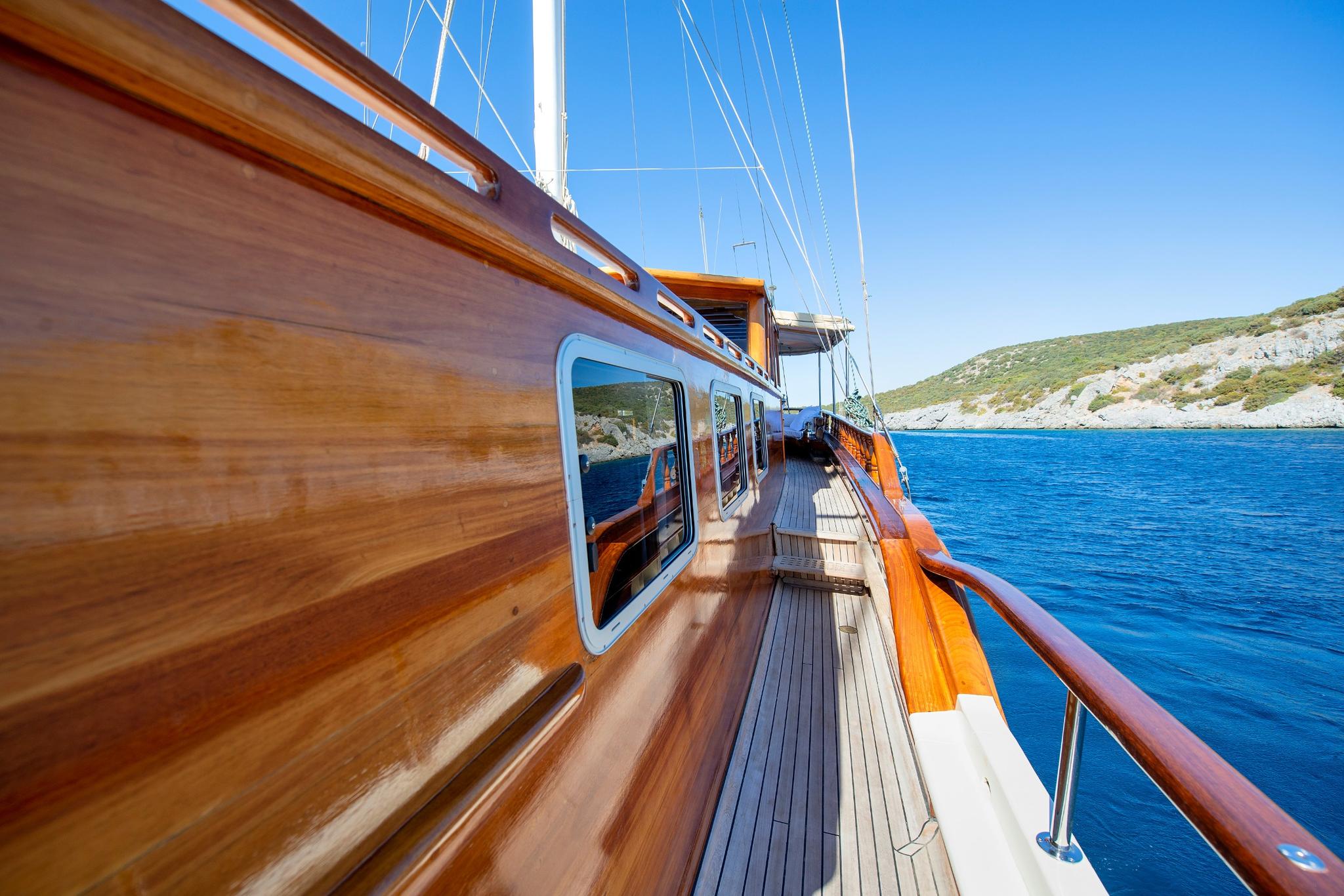 gulet side deck with teak planking, portholes, and wooden handrails overlooking blue waters