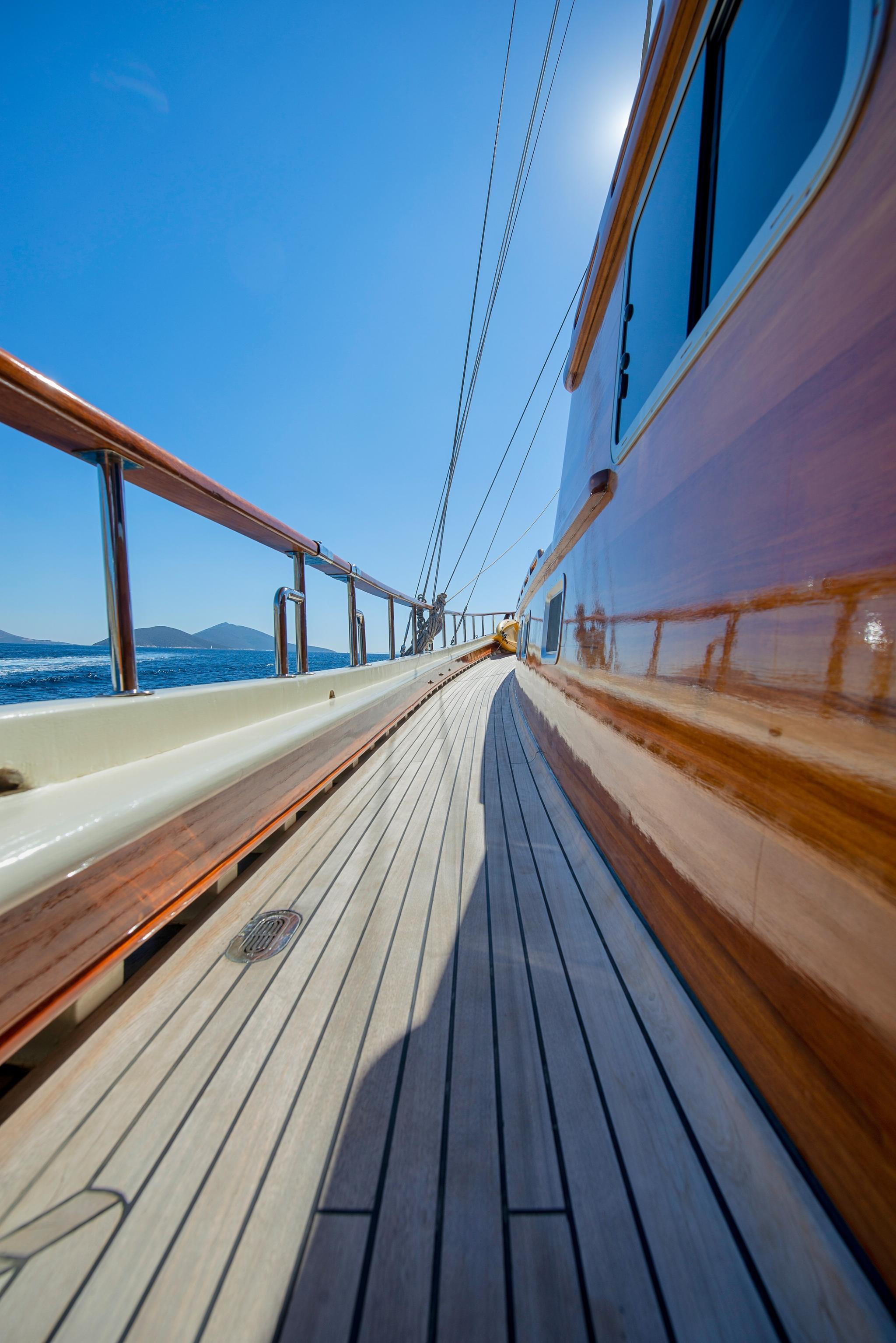 Gulet side deck with teak planking, steel railings and sailing rigging under blue sky