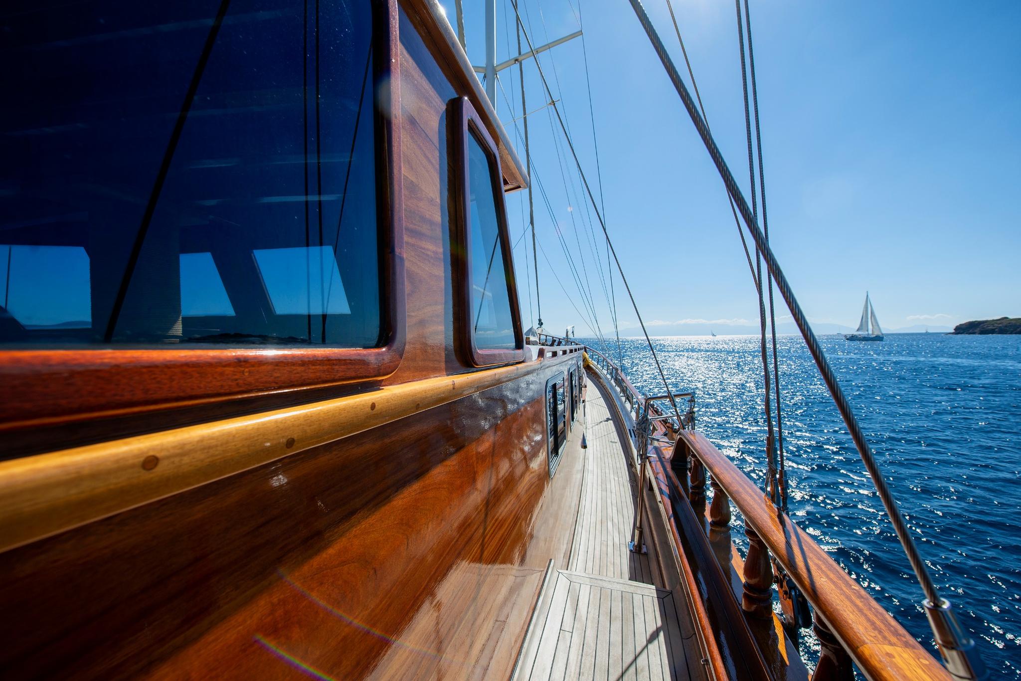 Gulet side deck with teak planking, wooden railings and sailing rigging against blue sea