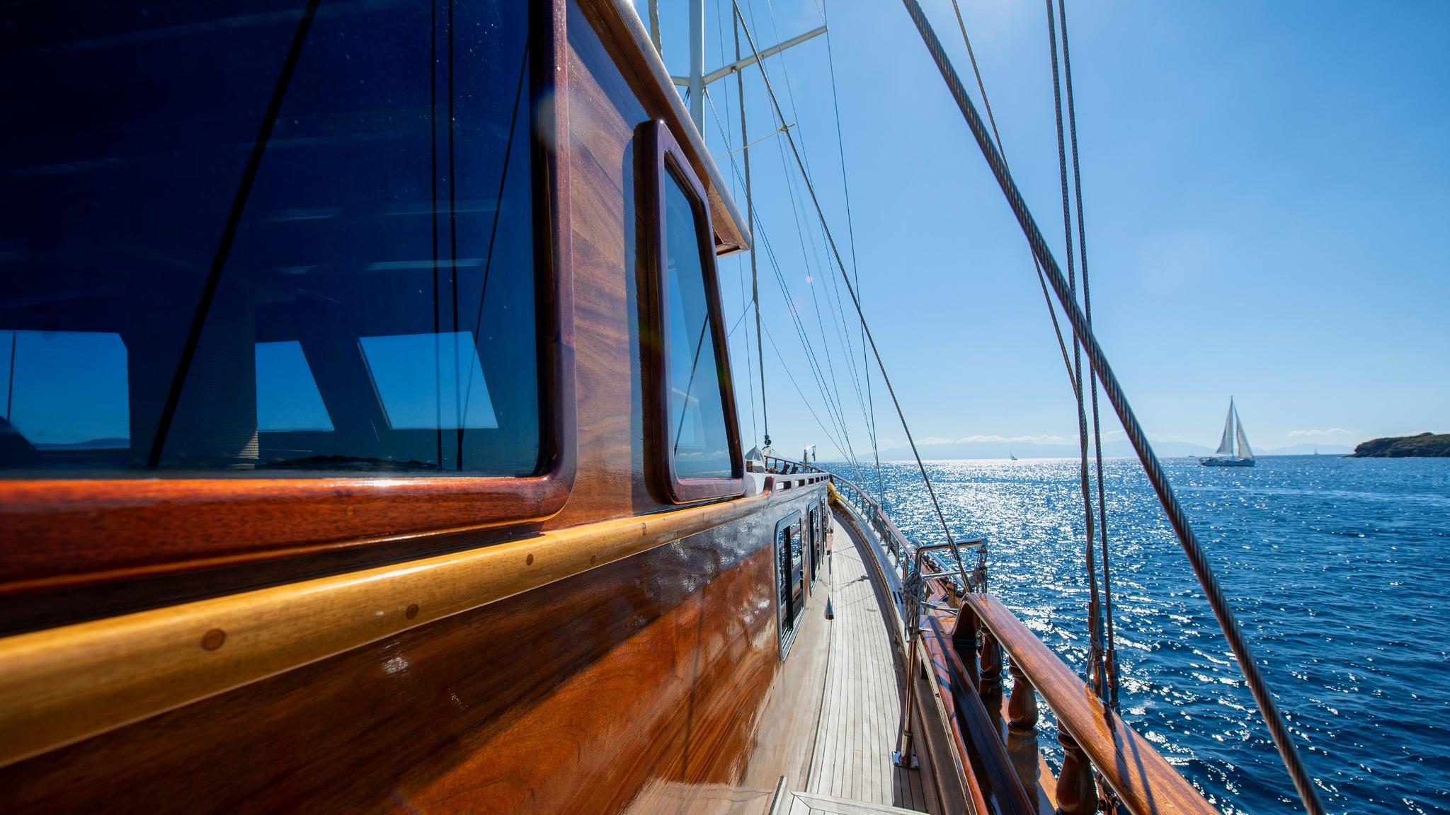 gulet side deck with wooden railings, rigging, and blue ocean view