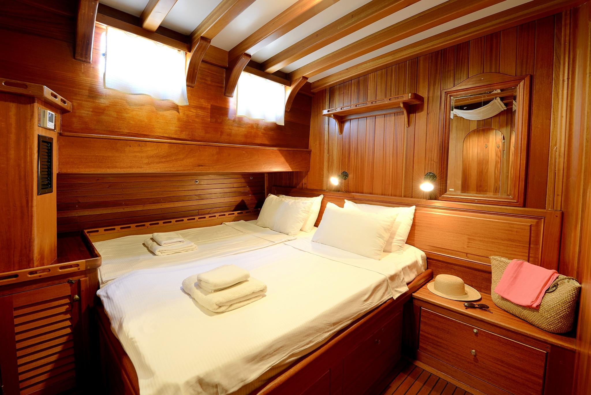 yacht guest cabin featuring double bed with white linens and rich teak wood paneling