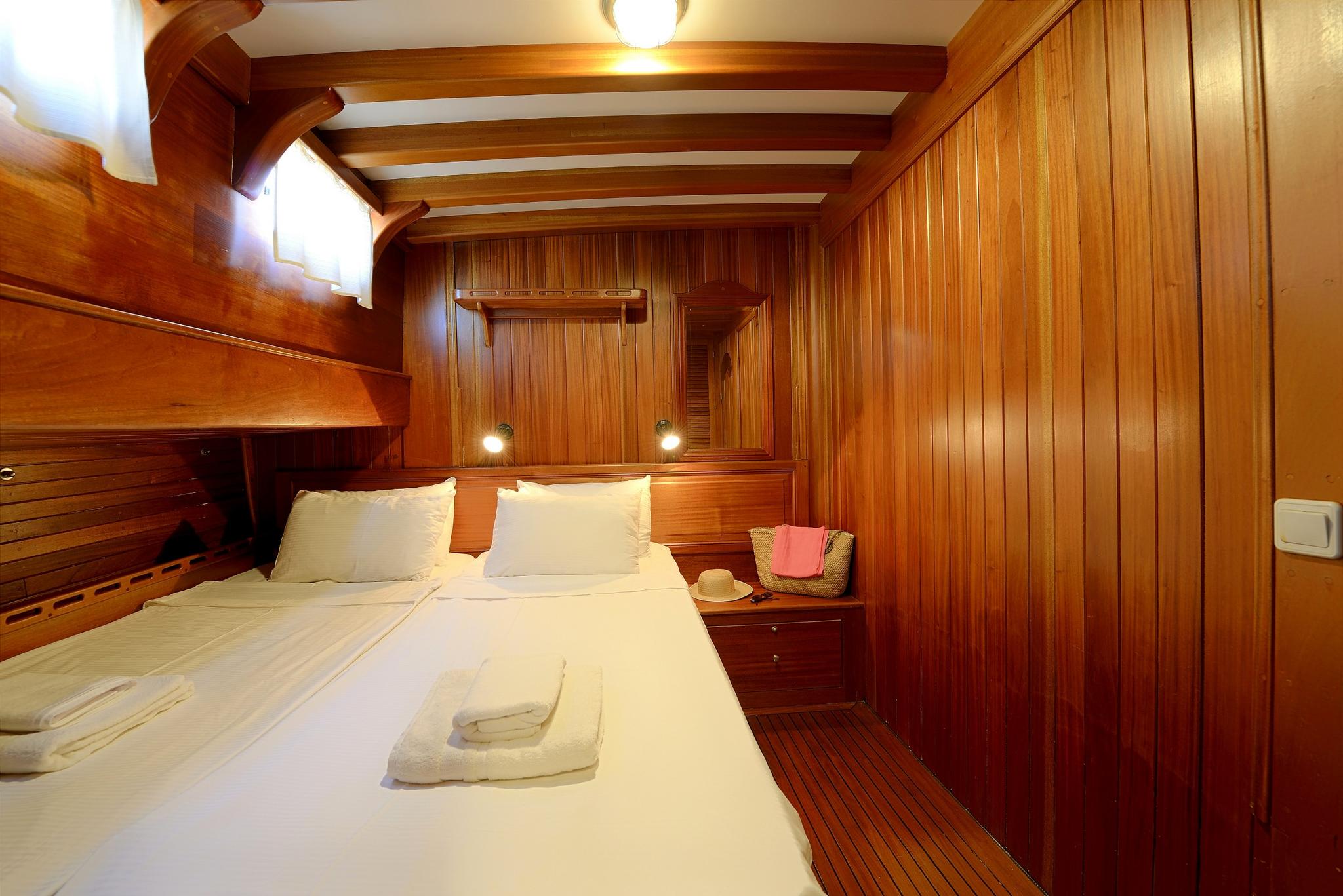 yacht guest cabin interior with double bed, wood paneled walls and built-in nightstand