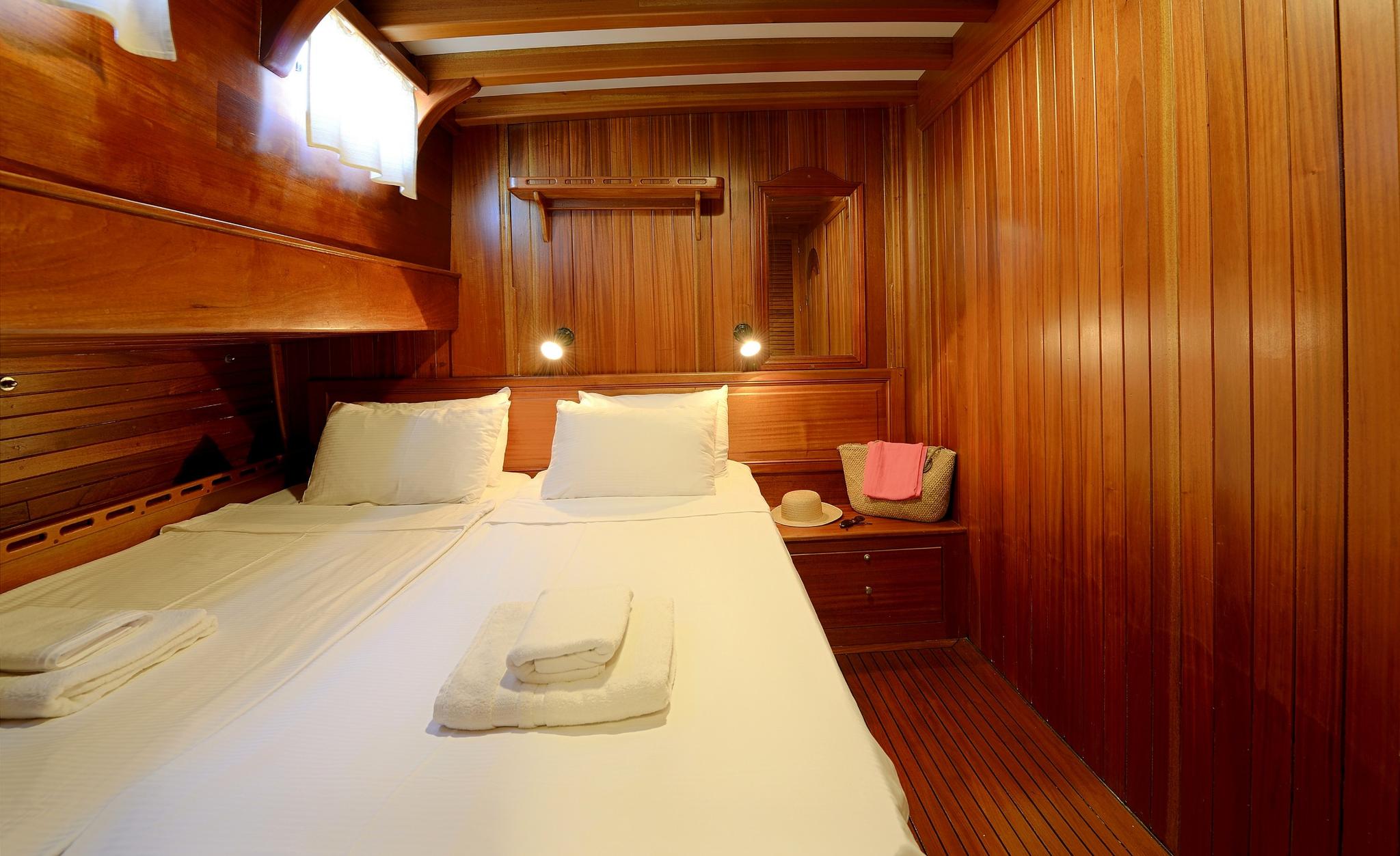 yacht guest cabin featuring double bed with white linens and rich teak paneling