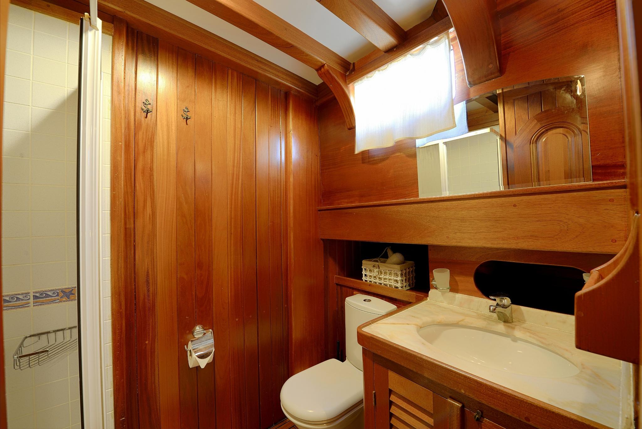 yacht bathroom interior with wooden paneling, toilet, marble sink counter and shower enclosure