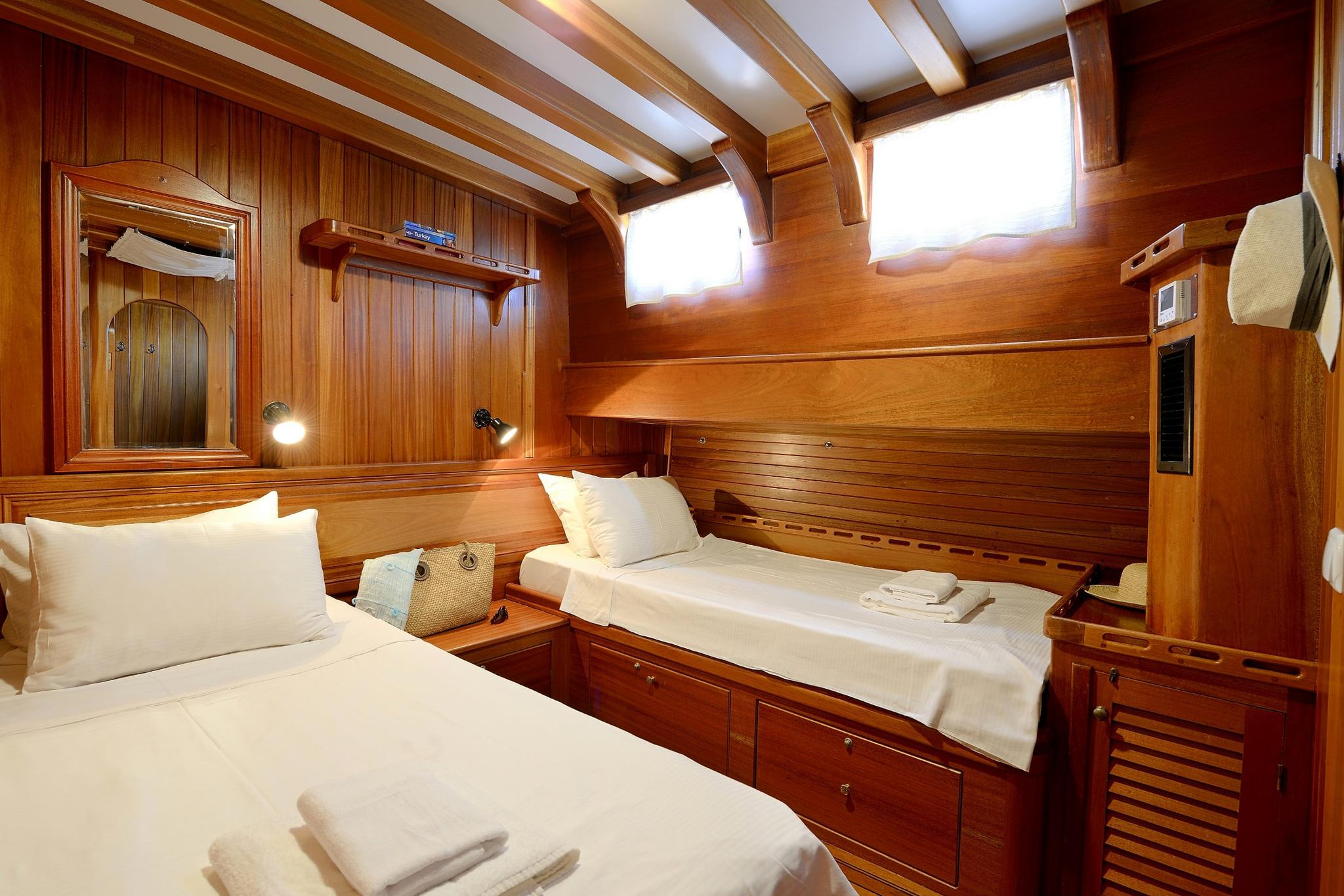 yacht guest cabin with two single beds, teak paneling, reading lights and storage drawers