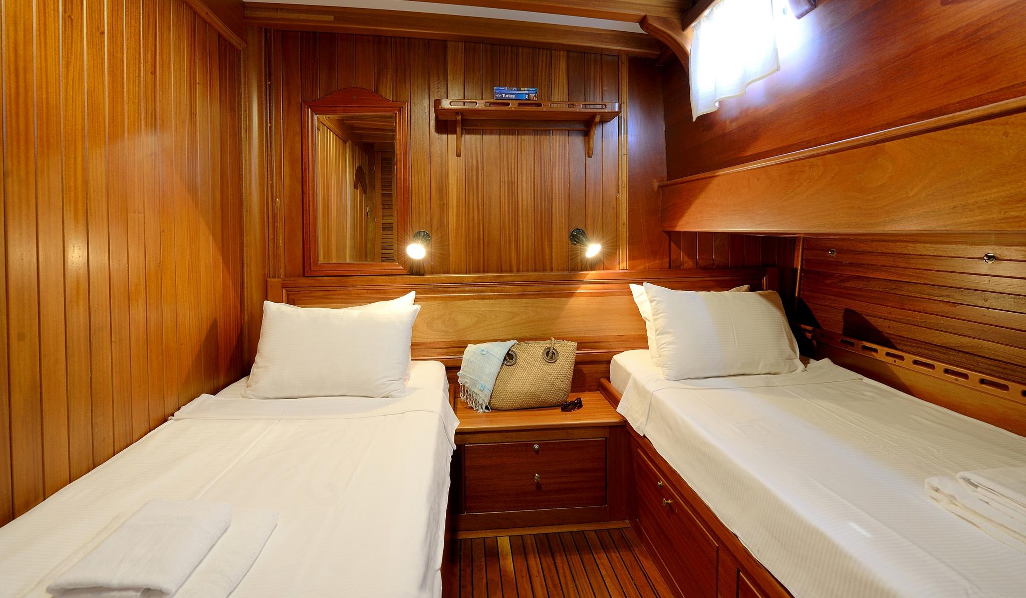 yacht twin cabin interior with two single beds, wooden walls, reading lights and storage