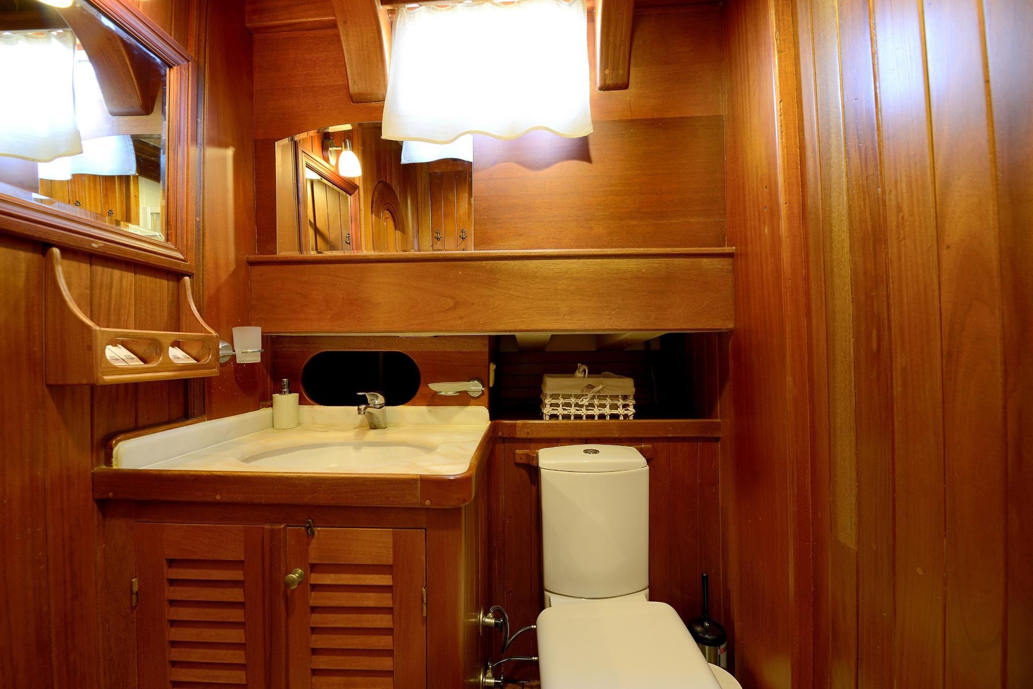 compact yacht bathroom featuring teak wood paneling, white sink, toilet and built-in storage