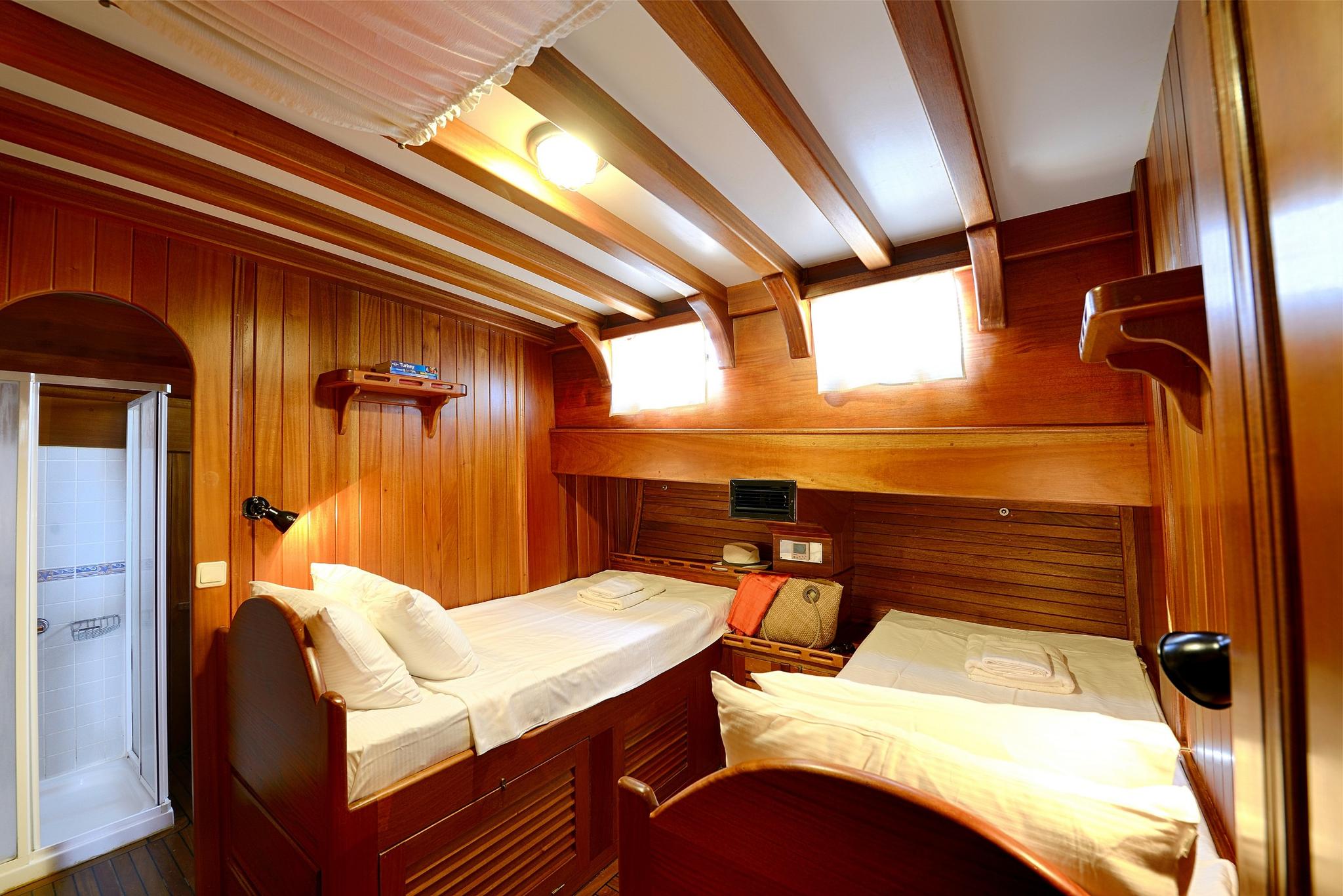 yacht twin cabin featuring two single beds with white linens and rich teak wood paneling