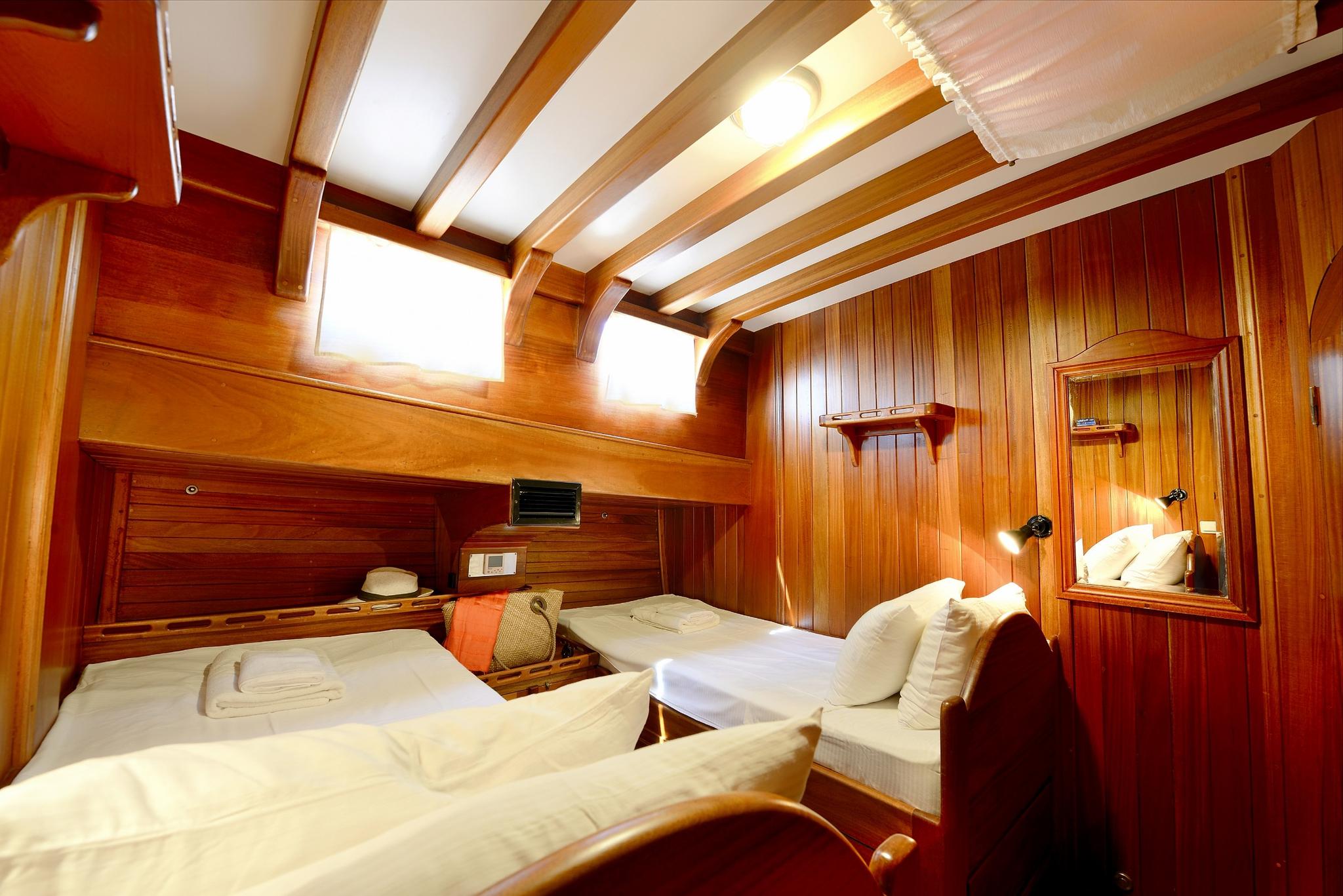 Twin cabin with two single beds, rich wooden paneling, exposed ceiling beams and portholes