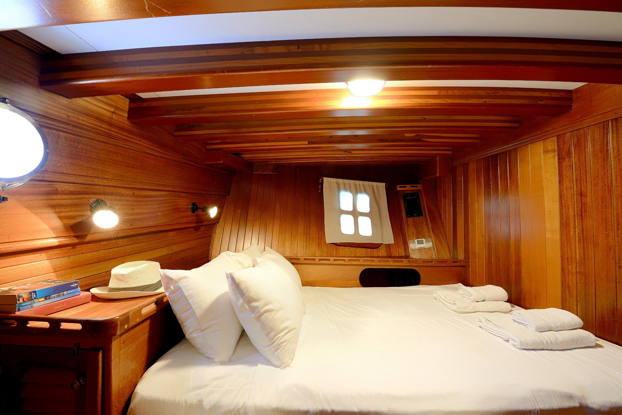 yacht guest cabin with white bedding, wooden walls, porthole window and ceiling beams