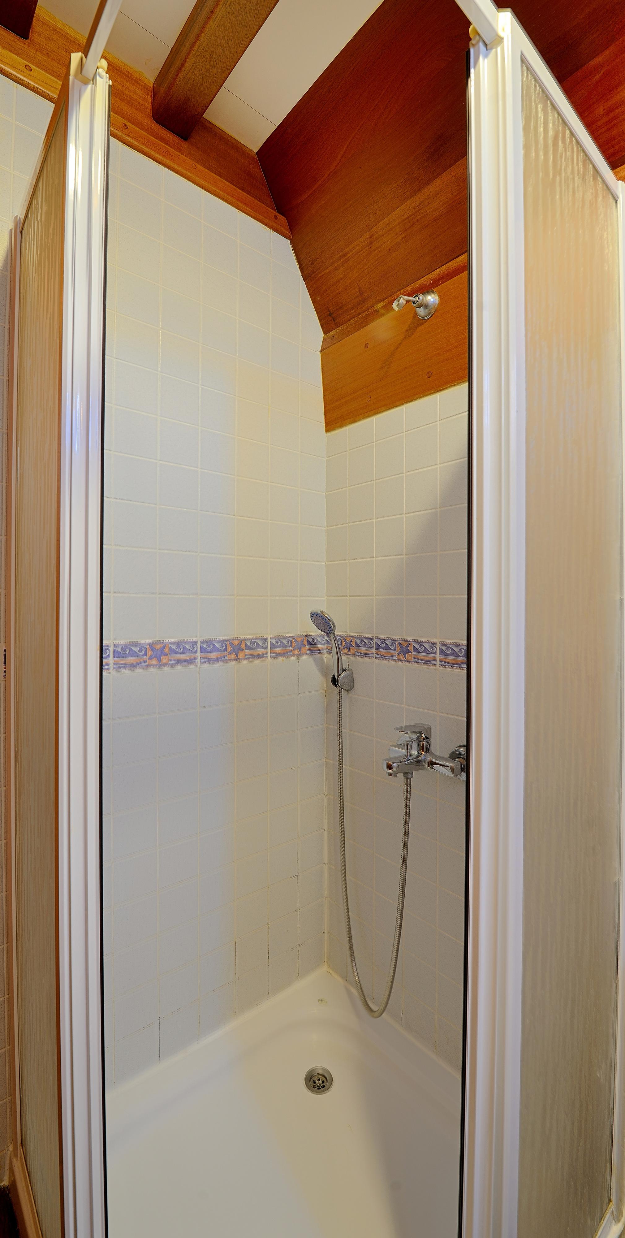 compact yacht bathroom shower stall with white tiles and decorative border