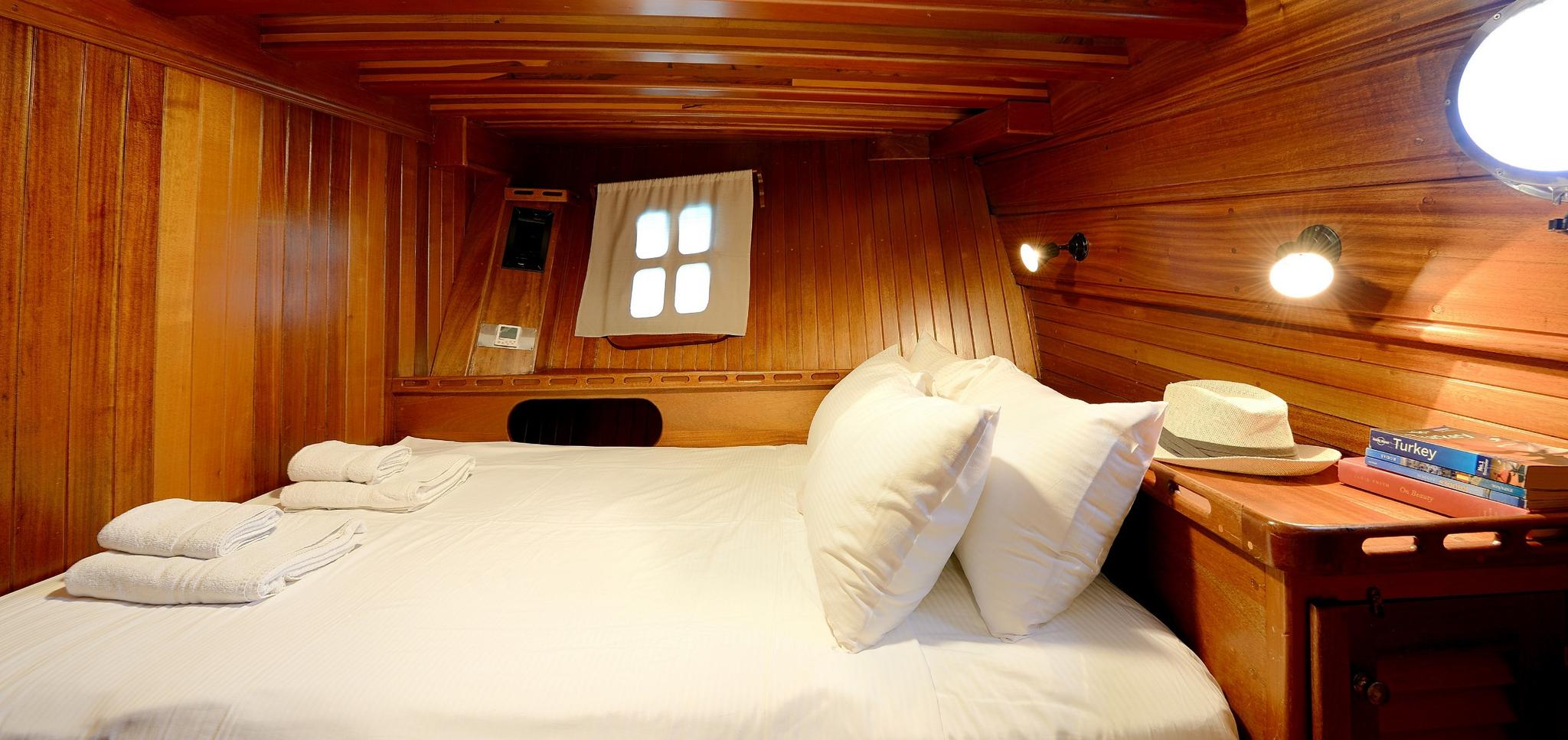 yacht guest cabin featuring double bed with white linens and rich wooden interior paneling